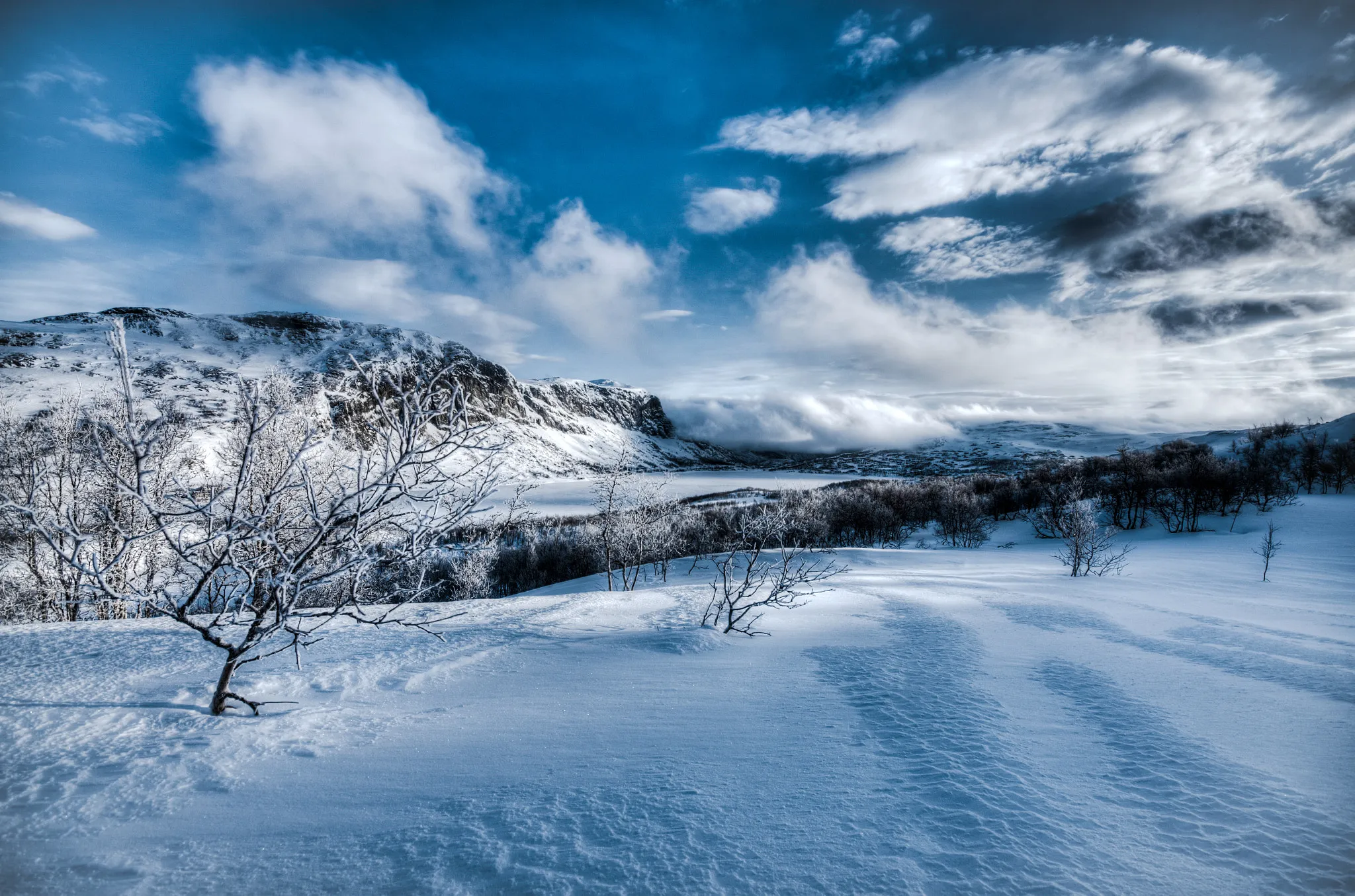 Photo showing: 500px provided description: Otr?vatnet is the frozen lake visible in the middle of the photo. I grabbed this on the way down from the mountain after four days of cross country skiing. The weather was changing a lot, with lots of wind and clouds rolling over us. Made for some fun photography, and cold fingers! I could probably have spent some more time evening out the sky and clouds, and if I had the opportunity I would probably have altered the composition slightly, but overall I'm fairly happy with the result. [#frozen ,#mountains ,#winter ,#clouds ,#snow ,#scandinavia ,#norway ,#cross country skiing ,#Skarvheimen]