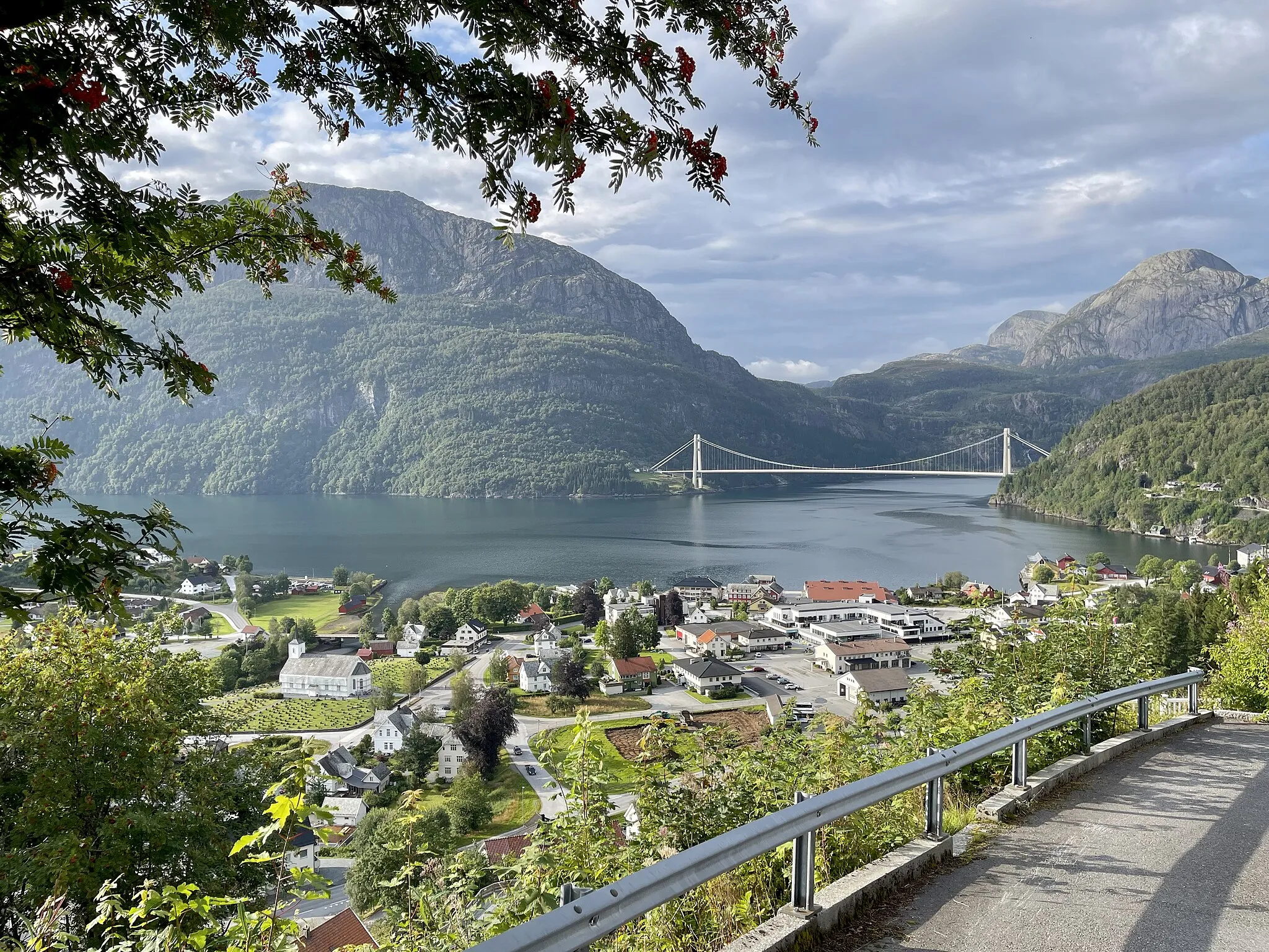 Photo showing: View from the Dalsåsen hill towards Dale in Sunnfjord, the administrative centre of the Fjaler municipality on the West Coast of Norway. Also the Dallsfjorden fjord, the Dalsfjord Bridge, mountains in the Askvoll municipality north of the fjord, etc. Photo taken on a summer's day in August 2021.