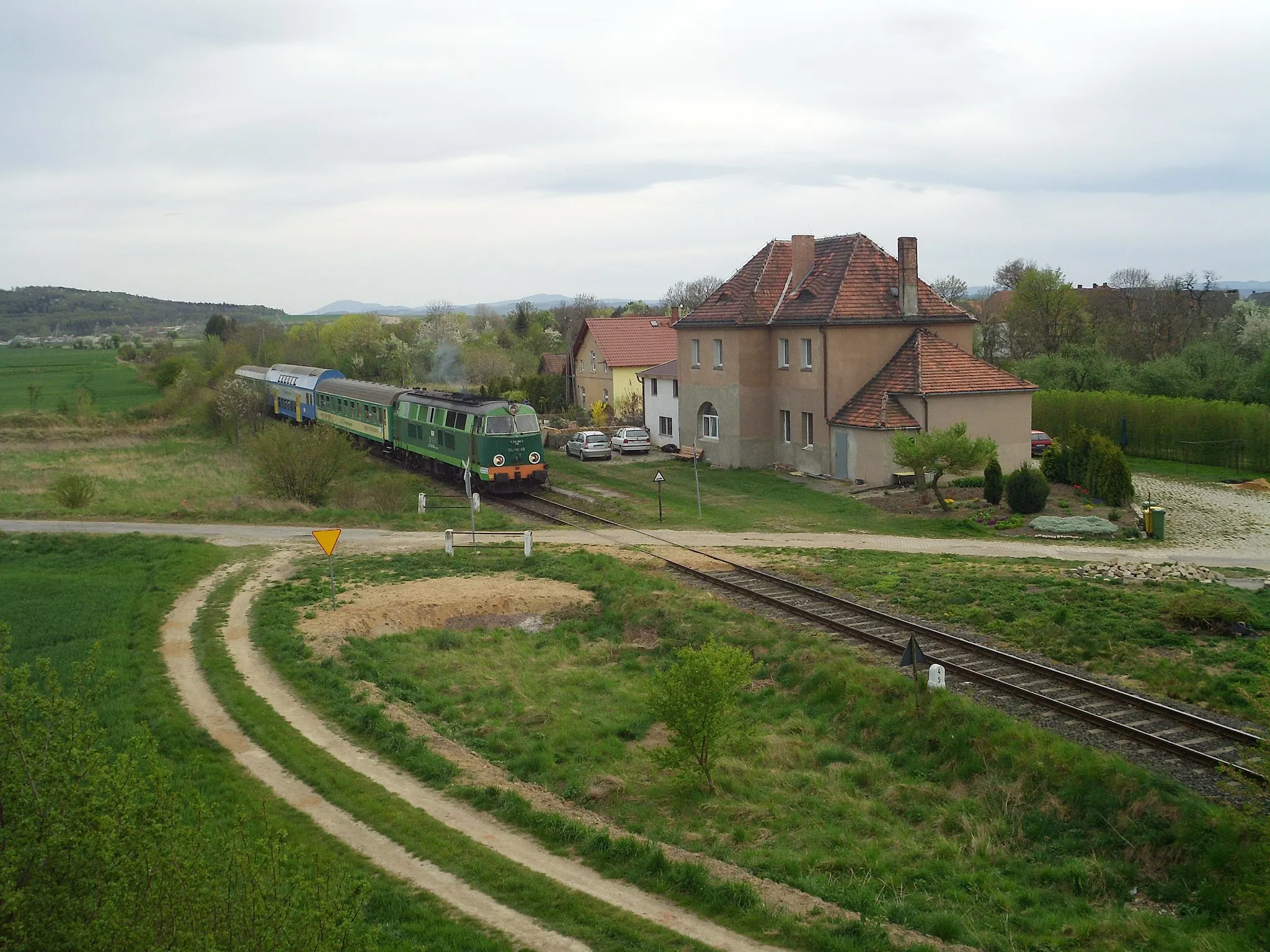 Photo showing: Tourist train headed by a diesel engine SU45-115 in front of a former station building in Siekierzice, Poland, on a freight line from Jawor. The train is heading towards Jawor and the picture was taken from a road bridge.