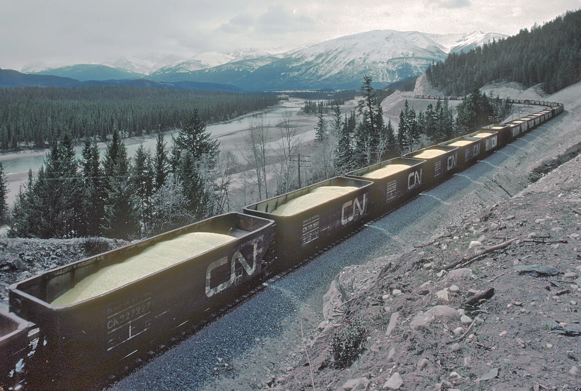 Photo showing: Roger Puta took this sequence of a westbound CN sulphur train powered by 3 SD40s about three miles east of Jasper, Alberta in May 1982.