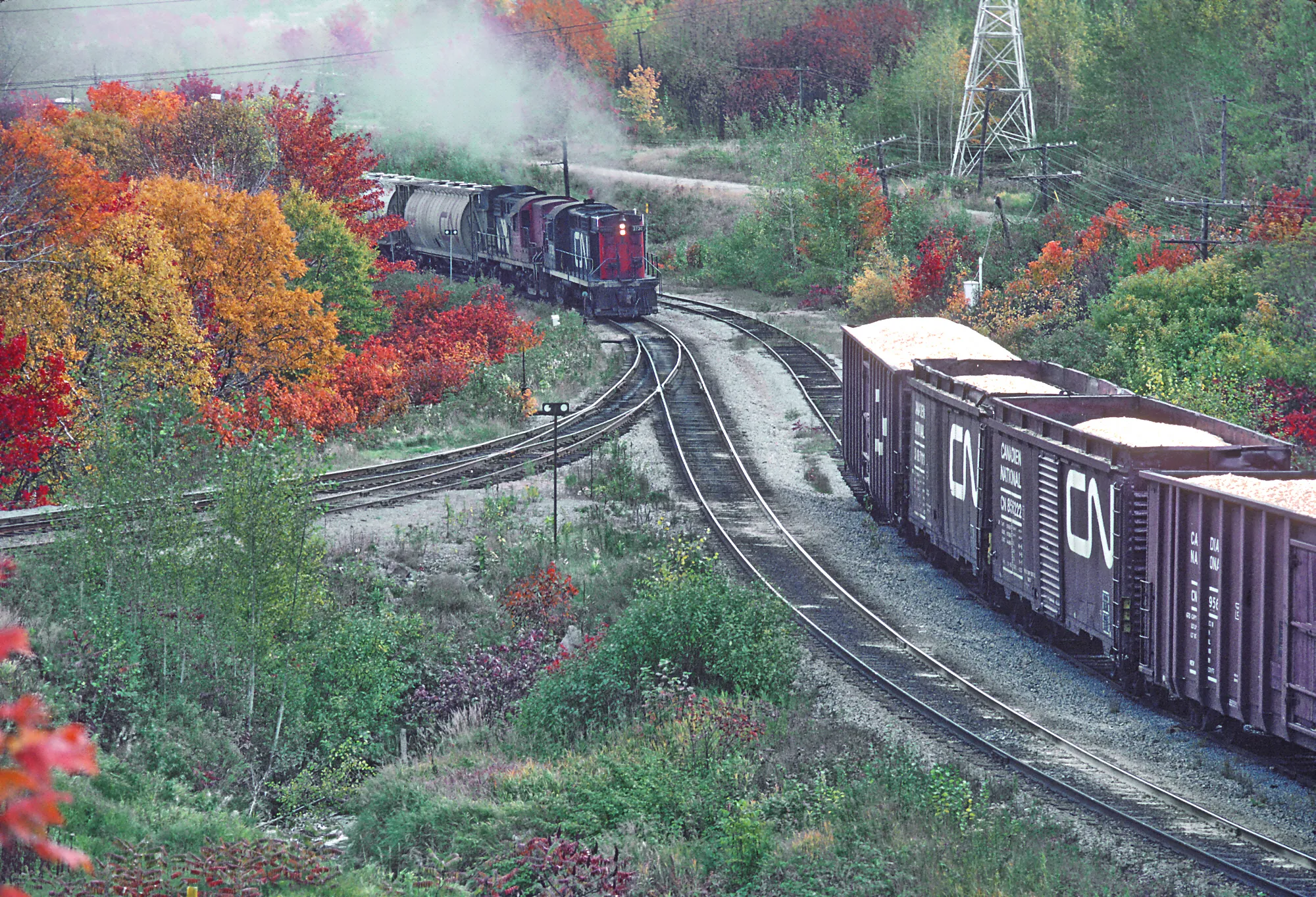 Photo showing: This is CN RS-3 3730 coming at you near Grand-Mère, Quebec in October 1981. The following comment is by kgmontreal, a member of Train Orders:

"Those 40' boxcars converted to woodchip cars were very common in Quebec, New Brunswick and Nova Scotia. Of course, the RS-18 units indicate that the photos were not taken in the western provinces. The train is westbound toward Shawinigan, QC from Garneau. The wye leads north to a mill in Grand Mère. The covered hoppers are for the Alcan aluminum smelter in Shawinigan. The photo was taken from the embankment at the CPR bridge to Grand-Mère over the CN mainline."
