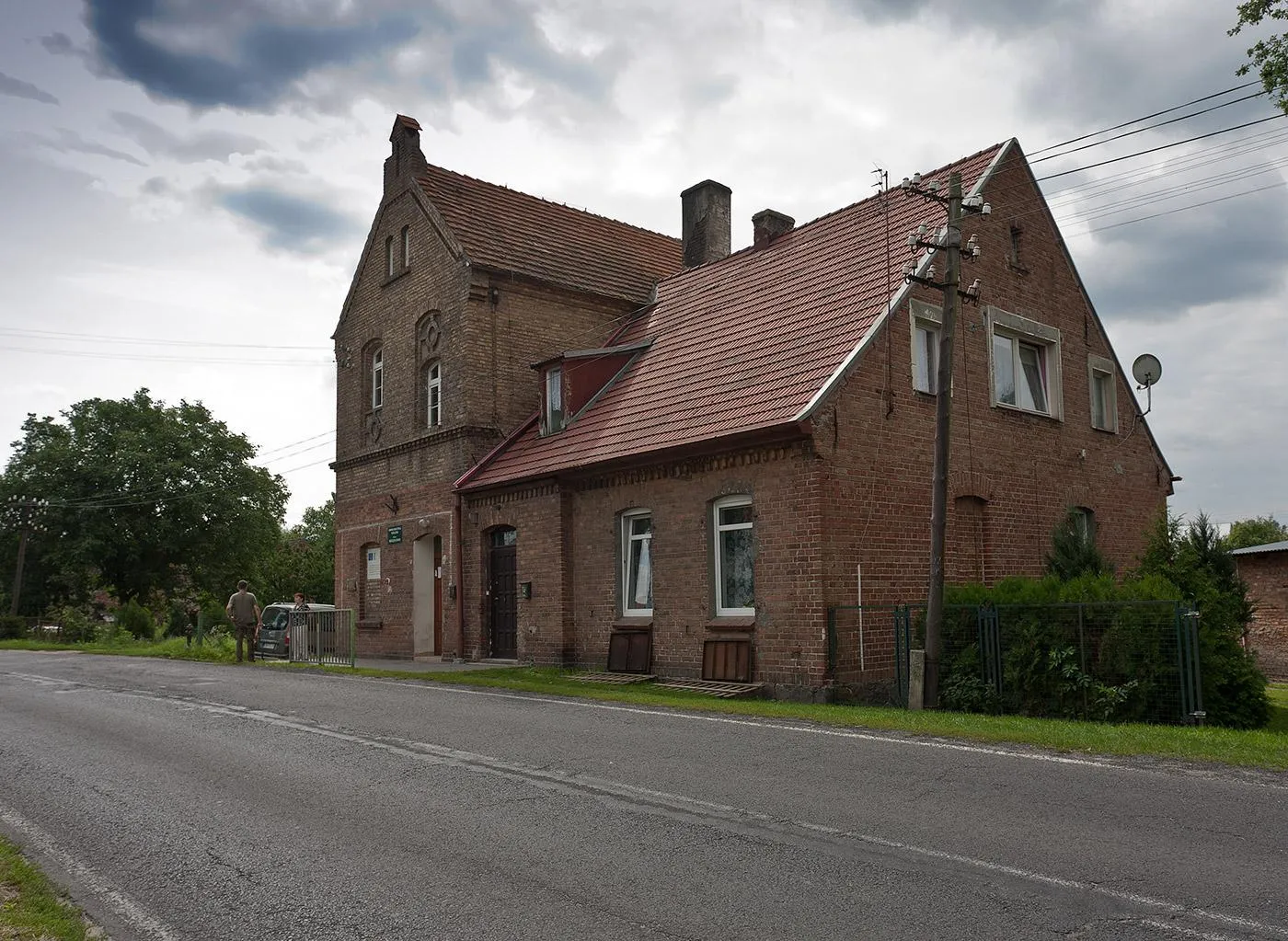 Photo showing: Budynek mieszkalny mieszczący na parterze filię biblioteki gminnej. Budynek widać, po odmiennym odcieniu cegły, że przebudowany. W kadrze Festung w akcji - próbuje wycyganić od pani bibliotekarki niskonakładowe, lokalne wydawnictwa:).