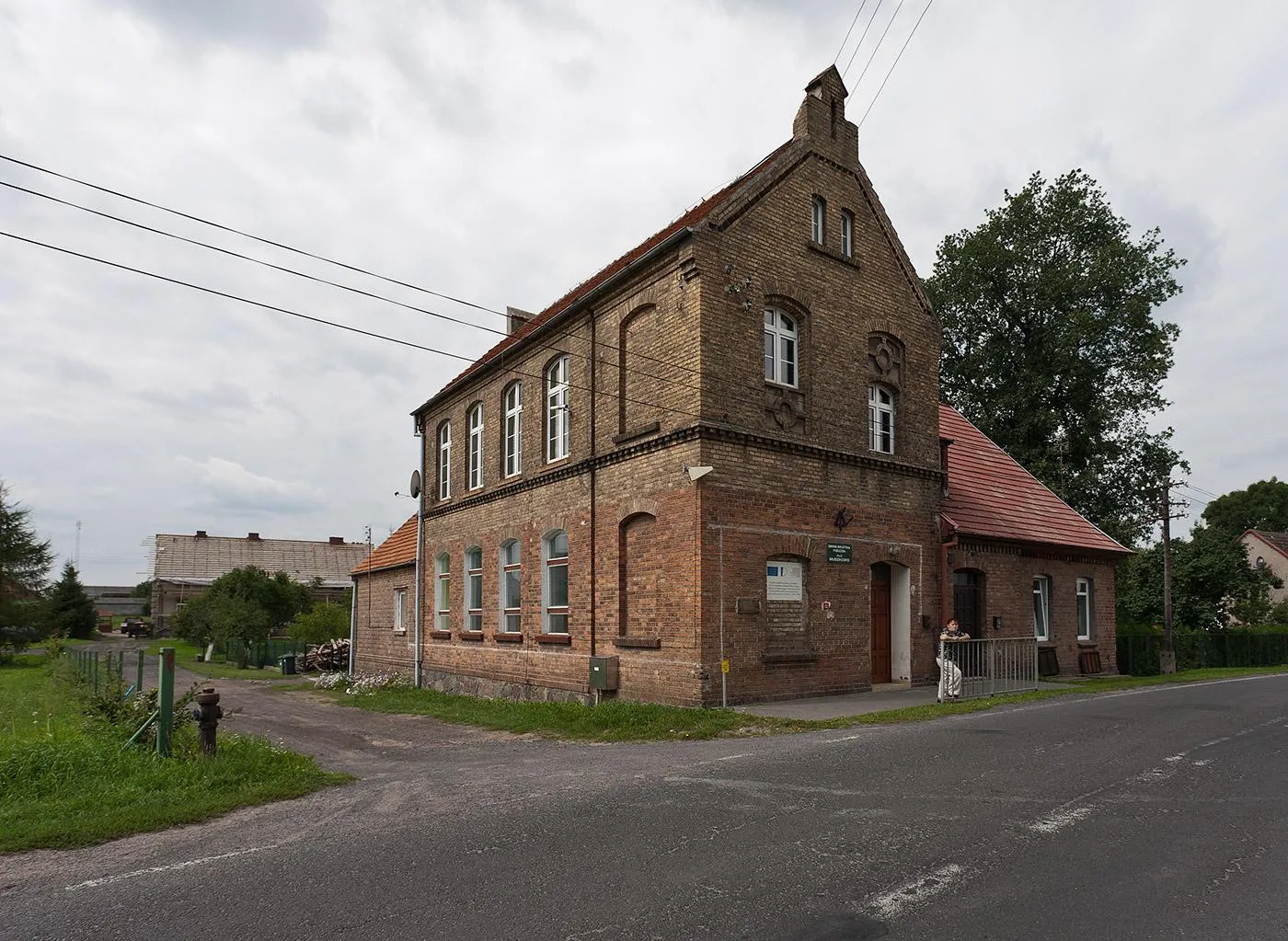 Photo showing: Budynek mieszkalny mieszczący na parterze filię biblioteki gminnej. Budynek widać, po odmiennym odcieniu cegły, że przebudowany.