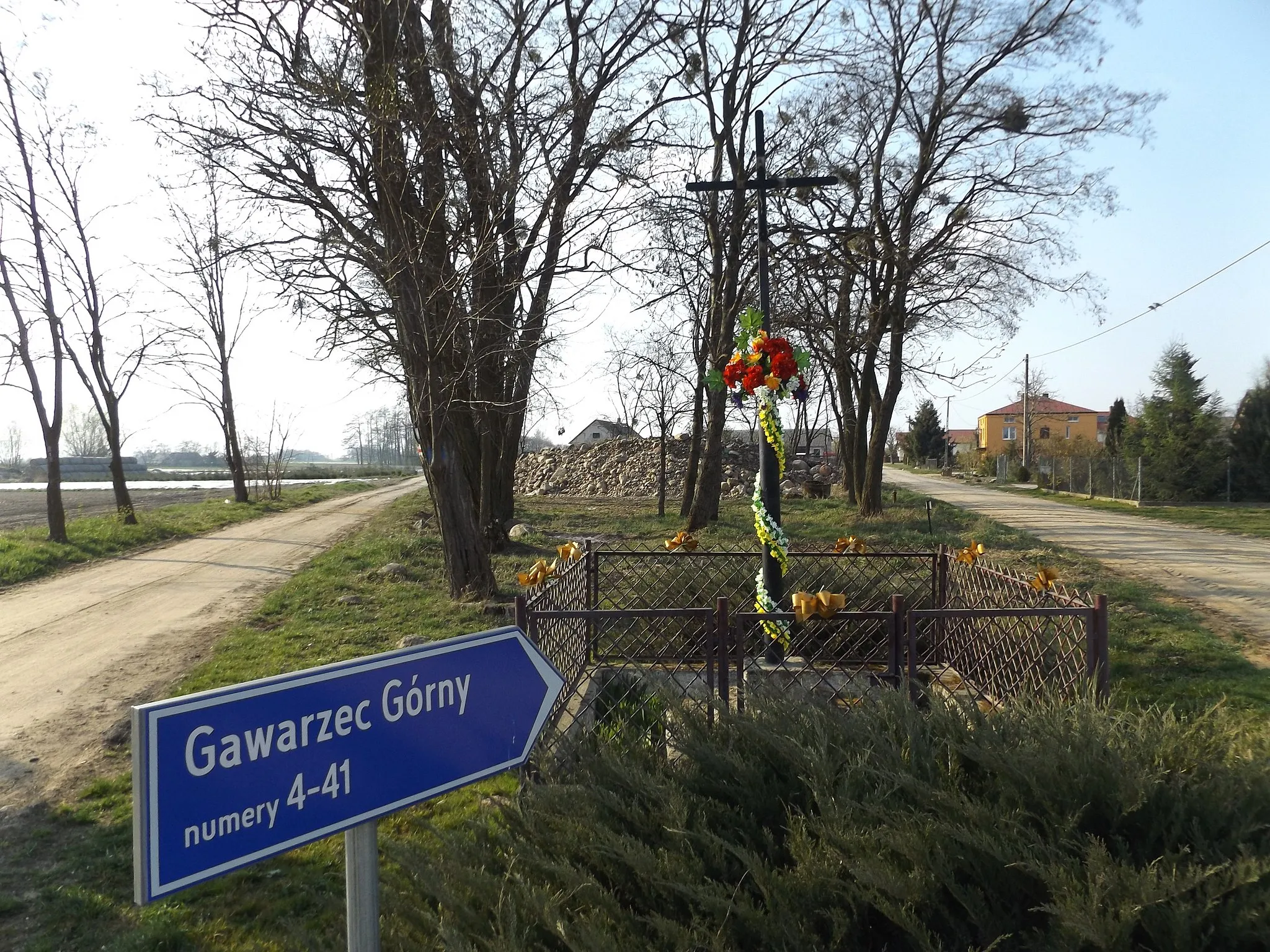 Photo showing: A metal cross with a metal figure, depicting the Crucified Jesus Christ; surrounded by a small, metal fence; located between two roads leading to the northwest (left to w:en:Gawarzec Dolny; right to centre of Gawarzec Górny), at the intersection of five roads on the border of the village in w:en:Gawarzec Górny (Czerwińsk nad Wisłą commune) in 2019 y.