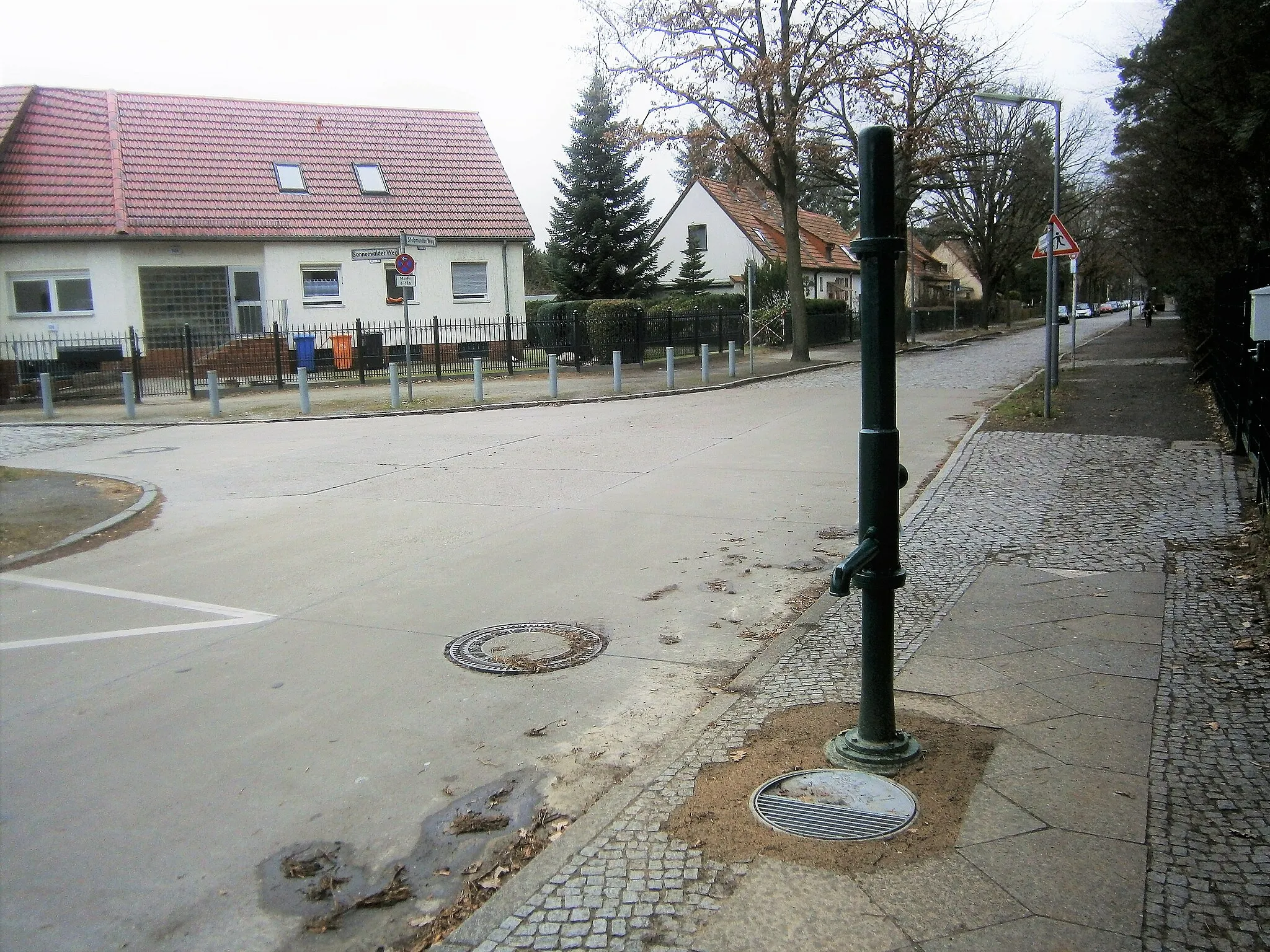 Photo showing: Der FSH-L-Brunnen 76 am westlichen Gehsteig Stolpmünder(NW-)Ecke Sonnenwalder Weg wurde 2018 aufgebaut und ersetzte einen älteren Brunnenkörper aus vier Rohrteilen.[1]. Im März 2019 befand sich am Schwengelgriff das Schild „Frisch gestrichen“ und der Fuß auf dem Sockelrohr mit dem Straßeneinlass unter dem Wasserauslauf waren in einer ungepflasterten Schüttung eingebracht. Die Brunnenstelle über der Quellbohrung wie vorher zwischen dem Pflasterrand und den Gehwegplatten gelegen, auch dei Ausrichtung von Rohr und Schwengel parallel zur Fahrbahn wie zuvor. Der Standort ist nach Landesliste der Anfrage[2] mit Brunnen Stolpmünder Weg (PLZ: 13503) beschrieben. Der Wasserfluss erfolgte sofort beim Pumpen. Am Mittelteil der Säule ist der Wasseraustritt am Ansatz der langen Hülse verschraubt.   Das anliegende Grundstück an der Brunnenseite gehört zur Ellef-Tingnes-Schule (Standort: Im Erpelgrund 11 - 17), südlich anschließend die Waldkirche (39/43 mit Kita 37/35). Hinter beiden Grundstücken folgt ein Streifen Forst und nach 180 Metern die Landesgrenze zu Stolpe-Süd.