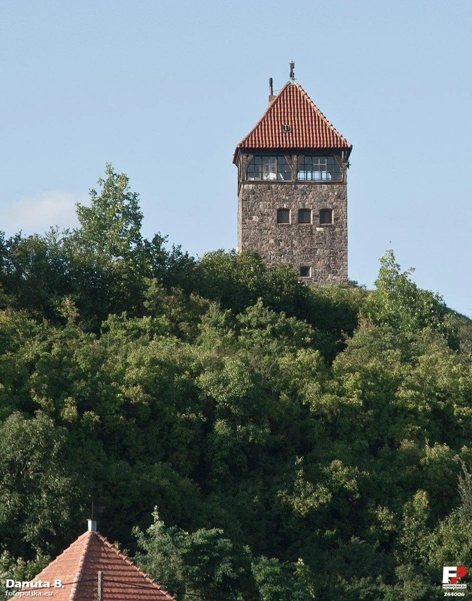 Photo showing: Zbliżenie na wieżę widokową z drugiego brzegu Warty. Na pierwszym planie czubek najwyższego dachu we wsi. Teren wznosi się, tworząc wąwozy. Wieża stoi na małej wyspie płaskiego terenu, tyle, że da się ja wygodnie obejść. O wjeździe samochodem nie ma mowy. Na górze, tam, gdzie okna jest jedno duże pomieszczenie z komikiem. A widok przecudny.