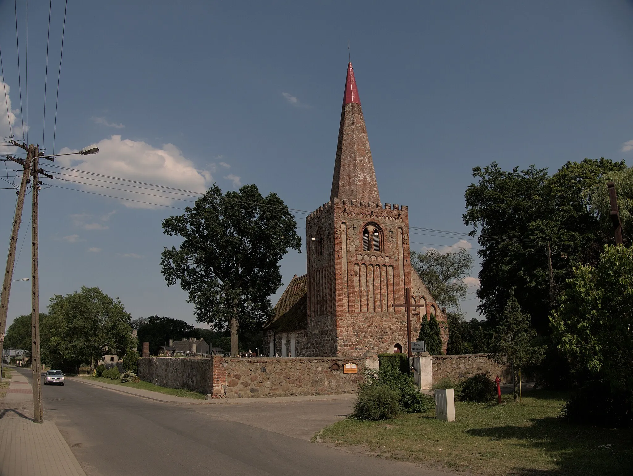 Photo showing: Blick auf die Dorfkirche Nowielin von der davorliegenden Kreuzung gesehen, Kirchturm und Kirchhof-Mauer.