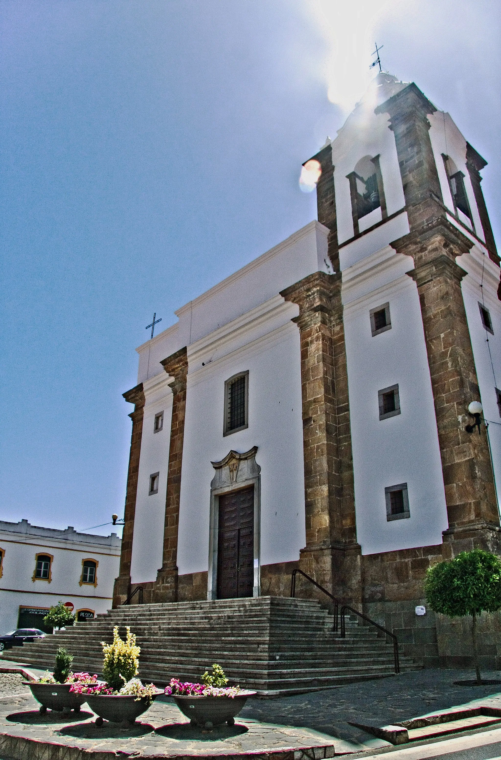 Photo showing: A escolha de Santo Ildefonso (monge e abade do mosteiro beneditino de Toledo, e depois bispo da mesma cidade, que viveu no século VII) como padroeiro da paróquia de Almodôvar constitui um interessante reflexo da presença da espiritualidade monástico - militar no Baixo Alentejo, difundida pelos freires da Ordem de Avis que seguia a Regra de São Bento.
Porém, a primitiva igreja matriz desta vila, pertencente em tempos ao padroado real, foi doada por D. Dinis, no ano de 1297, à Ordem de Santiago. Esta teve aqui uma das suas colegiadas, formada por um prior e três beneficiados.
O templo actual, traçado em 1592 pelo arquitecto Nicolau de Frias, constitui um exemplo muito elaborado da tipologia de “igreja-salão”, com três naves de quatro tramos cobertas de abóbadas, revelando grande sentido de unidade espacial. O desenho rigoroso da lanimetria, o ritmo da composição dos alçados e a própria atenção conferida ao tratamento dos pormenores, como as seis colunas toscanas em que assentam as arcarias de vulto perfeito, são bem reveladores do sentido de depuração classicizante atingida por este modelo nos finais do século XVI, em consonância com a austeridade da Contra-Reforma.
D. João V determinou uma remodelação parcial do edifício, assim descrita em 1747 pelo Padre Luís Cardoso: “porque a capela-mor se achava arruinada, e por sua pequenez fica imperfeito o edifício da igreja, que é o maior templo desta
comarca, foi Sua Majestade servido mandar pelo Tribunal da Mesa da Consciência, e Ordens, se derrubasse, e se fizesse regular ao restante da igreja, e se acrescentasse tribuna, que de presente se anda fazendo”. Estas obras vieram a ser completadas com a encomenda à oficina do entalhador eborense Sebastião de Abreu do Ó dos sumptuosos altares de talha dourada e policromada da nave, cuja riqueza denota pujança das diversas confrarias e irmandades da matriz.
Nos séculos XIX e XX realizaram-se outras intervenções de vulto que modificaram substancialmente a fábrica maneirista, a última das quais teve lugar na década de 1950. Data de então o painel de Severo Portela, representando o Baptismo de Cristo no Jordão, que ornamenta o baptistério.
A paróquia de Almodôvar conserva na igreja um importante acervo de alfaias litúrgicas, em parte oriundo do antigo Convento de Nossa Senhora da Conceição da mesma vila, que pertenceu à Ordem Terceira de São Francisco.
JOSÉ ANTÓNIO FALCÃO www.cm-almodovar.pt/turismo/locais_almodovar.htm

See where this picture was taken. [?]