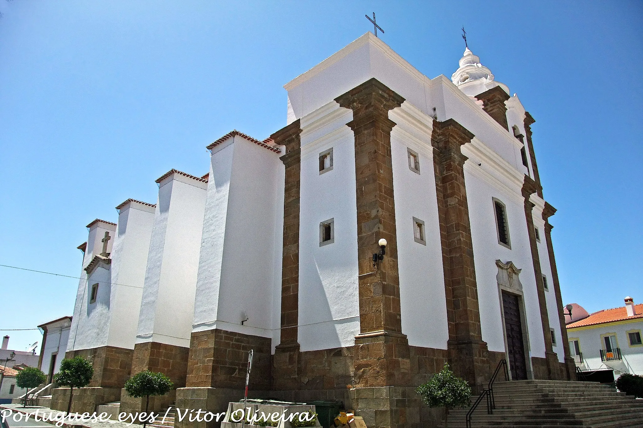 Photo showing: A escolha de Santo Ildefonso (monge e abade do mosteiro beneditino de Toledo, e depois bispo da mesma cidade, que viveu no século VII) como padroeiro da paróquia de Almodôvar constitui um interessante reflexo da presença da espiritualidade monástico - militar no Baixo Alentejo, difundida pelos freires da Ordem de Avis que seguia a Regra de São Bento.
Porém, a primitiva igreja matriz desta vila, pertencente em tempos ao padroado real, foi doada por D. Dinis, no ano de 1297, à Ordem de Santiago. Esta teve aqui uma das suas colegiadas, formada por um prior e três beneficiados.
O templo actual, traçado em 1592 pelo arquitecto Nicolau de Frias, constitui um exemplo muito elaborado da tipologia de “igreja-salão”, com três naves de quatro tramos cobertas de abóbadas, revelando grande sentido de unidade espacial. O desenho rigoroso da lanimetria, o ritmo da composição dos alçados e a própria atenção conferida ao tratamento dos pormenores, como as seis colunas toscanas em que assentam as arcarias de vulto perfeito, são bem reveladores do sentido de depuração classicizante atingida por este modelo nos finais do século XVI, em consonância com a austeridade da Contra-Reforma.
D. João V determinou uma remodelação parcial do edifício, assim descrita em 1747 pelo Padre Luís Cardoso: “porque a capela-mor se achava arruinada, e por sua pequenez fica imperfeito o edifício da igreja, que é o maior templo desta
comarca, foi Sua Majestade servido mandar pelo Tribunal da Mesa da Consciência, e Ordens, se derrubasse, e se fizesse regular ao restante da igreja, e se acrescentasse tribuna, que de presente se anda fazendo”. Estas obras vieram a ser completadas com a encomenda à oficina do entalhador eborense Sebastião de Abreu do Ó dos sumptuosos altares de talha dourada e policromada da nave, cuja riqueza denota pujança das diversas confrarias e irmandades da matriz.
Nos séculos XIX e XX realizaram-se outras intervenções de vulto que modificaram substancialmente a fábrica maneirista, a última das quais teve lugar na década de 1950. Data de então o painel de Severo Portela, representando o Baptismo de Cristo no Jordão, que ornamenta o baptistério.
A paróquia de Almodôvar conserva na igreja um importante acervo de alfaias litúrgicas, em parte oriundo do antigo Convento de Nossa Senhora da Conceição da mesma vila, que pertenceu à Ordem Terceira de São Francisco.
JOSÉ ANTÓNIO FALCÃO www.cm-almodovar.pt/turismo/locais_almodovar.htm

See where this picture was taken. [?]