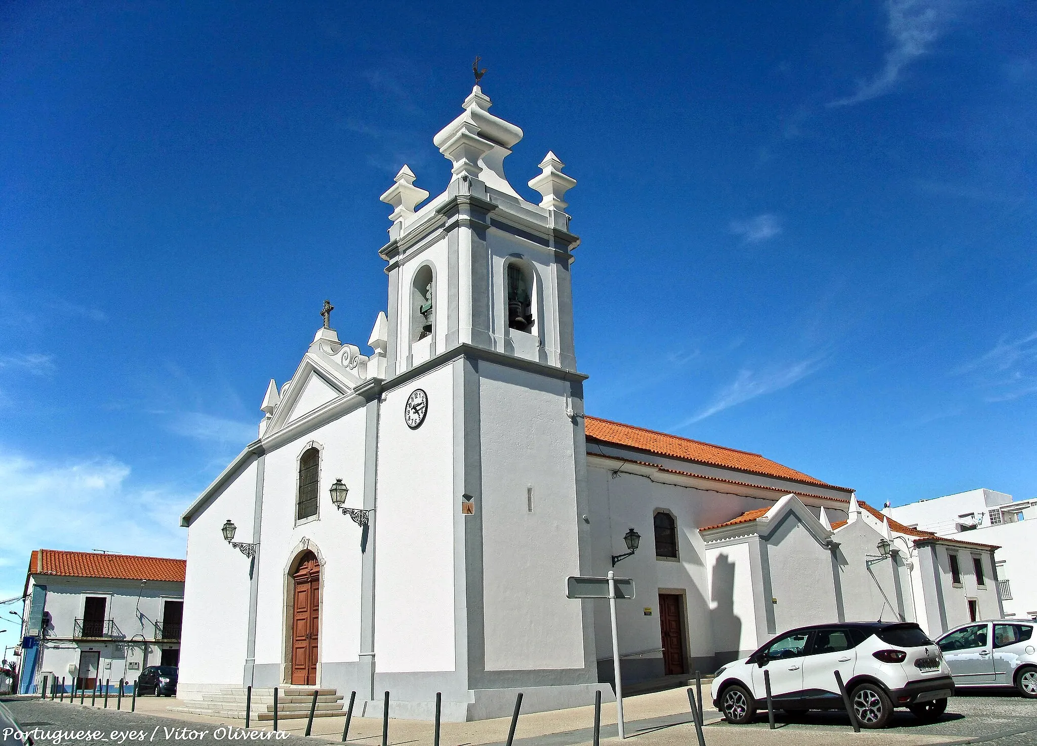 Photo showing: Degradada e a precisar de obras em 1482, é possível que a construção da igreja de Nossa Senhora da Abendada remonte a meados do século XV. Em 1513, D. Jorge (mestre da Ordem de Santiago), aquando da sua visitação, mandou reparar a igreja por apresentar alguma degradação: as pinturas murais estavam deterioradas, a pia baptismal era uma tina grande em barro e o corpo da igreja encontrava-se por ladrilhar.

No século XVI, passou a designar-se por igreja de Nossa Senhora da Assunção, e é também a partir desta centúria que começa a ser remodelada e ampliada, passando a adquirir progressivamente o traçado que actualmente a caracteriza.

O seu interior é constituído por um vestíbulo com paredes em madeira, nave única com cobertura em madeira de três panos, pintada com motivos geométricos simples. Sobre o espaço da entrada há um coro alto em madeira com balaustrada.

No lado esquerdo (evangelho) existe uma capela transformada em baptistério, com uma tina grande de pedra em forma de cálice e, na parede, uma pintura sobre madeira do século XVI, em estilo Maneirista, que representa o Pentecostes, cuja autoria é atribuída a Fernão Gomes. A esta segue-se outra capela com altares em talha dourada que foi integralmente restaurada em 2013.

Os belos retábulos colaterais, esquerdo e direito, em talha dourada, também foram sujeitos a intervenções de conservação e restauro, durante o ano de 2013.

No lado direito (epístola) encontram-se duas capelas - simétricas às do lado norte, evangelho -. A primeira, da Irmandade das Almas, apresenta retábulo de talha dourada e é revestida a azulejos de padrão floral em azul e amarelo (datados de 1657), e foi restaura em 2011, a segunda tem igualmente retábulo em talha dourada, azulejos atribuídos aos séculos XVI, XVII e XX e foi restaura em 2013.

O altar-mor, cuja entrada é encimada por um arco de volta perfeita e um hábito da Ordem de Santiago, apresenta um retábulo de feição neoclássica onde se destacam duas belas estátuas que representam a Fé e a Esperança.

Na fachada exterior, podem ver-se, entre outros elementos, um hábito da Ordem de Santiago esculpido sobre a porta principal e uma janela com vitral. No campanário há a registar o mostrador de um relógio de sol, quatro janelas sineiras, quatro cornijas e um pináculo. O lado norte é ocupado pelo novo centro paroquial e residência do pároco e, no lado sul, podem ver-se, além dos elementos referidos, as paredes das capelas laterais e do escritório, com uma porta e duas janelas com vitrais.

Síntese de intervenções:

Em 1513, esta Igreja tinha cerca de 85 m2 de área total e continuava degradada e, entre 1525 e 1534, foi totalmente reconstruída e ampliada, ficando então com 194 m2 de área. Entre o século XVI e o século XVIII, sofreu várias intervenções, nomeadamente o acréscimo de dois anexos, a construção de capelas e o revestimento em azulejos. A maior alteração ocorreu, contudo, na década de 70, com a construção do centro paroquial e a habitação do pároco, que alterou a antiga feição da Igreja (a norte). www.cm-grandola.pt/frontoffice/pages/559?poi_id=294