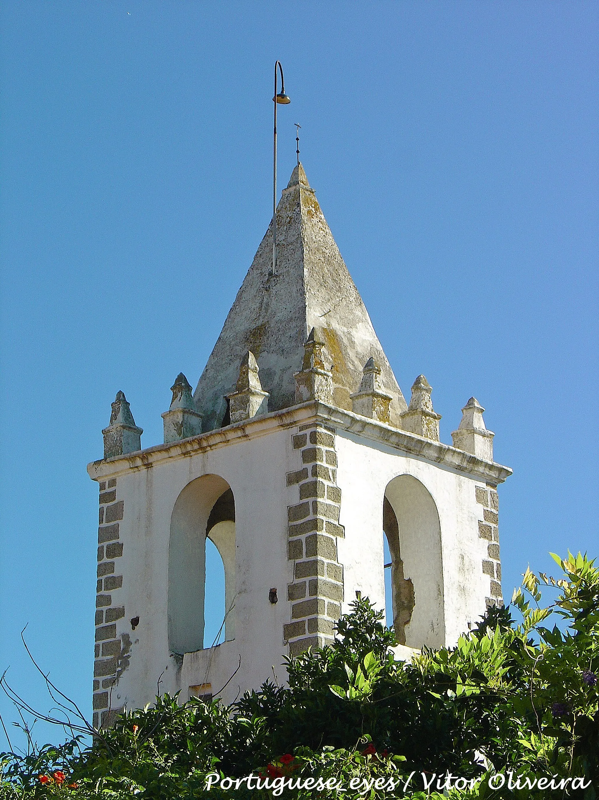 Photo showing: A Torre do Relógio, da qual não se sabe a idade, não foi construída para relógio, embora no séc. XVI tenha passado a ter essa função.
Tem uma estrutura quadrangular em alvenaria com quinais de granito, quatro olhais e um sino. Na cúpula tem uma pirâmide quadrangular, com doze pequenas pirâmides de igual desenho, no patamar. O antigo relógio está voltado a sudeste e o novo para sudoeste. O mostrador do relógio primitivo tem a data de 1570 mas, no reboco, imediatamente por baixo, está a data de 1741, que tanto pode ser da colocação do relógio como de alguma reparação na torre.
Antes de haver relógios, as torres tinham geralmente funções religiosas e cívicas. As primeiras consistiam em convocar os fiéis para os actos do culto, para as solenidades religiosas ou para os funerais; as segundas consistiam em alertar o povo em momentos de perigo ou para a difusão de outras mensagens.
A torre, que não é por essência um elemento do corpo do templo, pode inicialmente ter tido funções religiosas de apelo ou de aviso, por meio dos seus sinos. Há em Portugal várias igrejas antigas, cujas torres estão separadas dos templos por alguma conveniência. Esta hipótese encaixa numa outra respeitante à inexistência de torre na primitiva Igreja de Cabeço de Vide. Assim sendo, esta torre bem pode ter sido a torre da primitiva Igreja.
Era também a torre sineira que marcava o início e o termo dos trabalhos diários do campo (nascer e pôr-do-sol), a hora do jantar e o meio-dia.
Estes toques, em linguagem de fé, são chamados Angelus. www.jf-cabecodevide.pt/torre.htm

See where this picture was taken. [?]