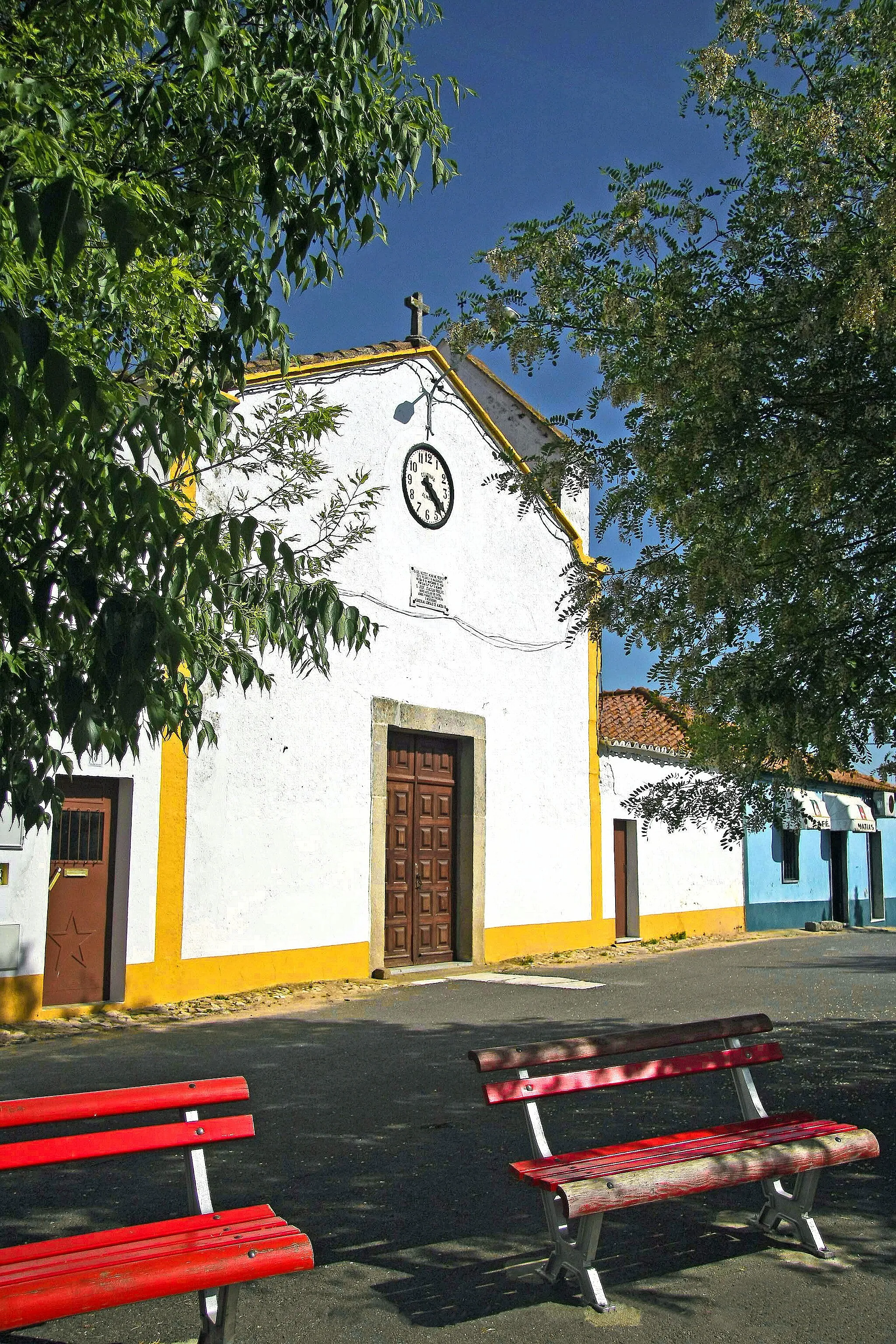 Photo showing: A igreja paroquial de Aguiar foi fundada em épocas muito remotas, possivelmente à sombra do padroado do rei D. Dinis e do donatário medieval Fernão Gonçalves Cogominho. Já é citada em documentos régios do ano de 1320 e o seu primeiro prior conhecido foi o bacharel da Sé de Évora Afonso Esteves. A igreja primitiva perdeu-se nos princípios do século XVI e, do período manuelino é a abside subsistente, que foi melhorada por determinação de D. Martinho, após a Visitação de 1534, tendo sido, então, recoberta a nave de travejamento de madeira e recomposto o alpendre da fachada, hoje desaparecido. Estava como seu reitor, na altura o P. João Lopes, sucedendo-lhe o humanista eborense Mestre André de Resende, que custeou a montagem do retábulo da capela - mor, infelizmente perdido em meados do século XVIII.
Teve as seguintes confrarias: Senhora da Assunção (titular), Senhora do Rosário, Senhora das Candeias, Almas e Senhor Jesus, Santo António e São Sacramento.
De frente ao ocidente e situada no antigo Rossio da vila, na passagem da Estrada Real, sofreu uma profunda alteração na fachada, em data imprecisa do século XVIII, que lhe modificou, estruturalmente, os primitivos volumes arquitectónicos. A sóbria e pobre obra subsistente, tem portal granítico, adintelado, frontão triangular, rematado por cruz de pedra, coruchéu no extremo norte e no oposto robusto campanário agudo, de alvenaria decorada por esgrafitos artísticos, com dois olhais e igual número de sinos de bronze fundido, estando o mais antigo, com grande cruz relevada, de andares e estrelóide, cronografado de 1772.
O actual sino das horas, que substituiu o primitivo, é moderno e foi colocado na altura de inauguração do relógio, precisamente no óculo de iluminação do edifício, tendo sotoposta, a lápida marmórea que assinalava o evento.
Na face sul da nave vê-se, obstruído, o portal gótico, relíquia pétrea de templete quatrocentista.
Maior curiosidade conserva a abside, contemporânea do priorado de mestre André de Resende, rasgada por frestas graníticas e gigantes esquinados, com remates de gárgulas de mármore, do tipo canhão.
No lado oposto fica a sacristia, da mesma época e de secção cupular, com telhado de linhas radiadas, envolvido por pináculos esferóides.
Interiormente, o corpo da nave está disposto em planta rectangular e com abobadilha redonda, púlpito, capela baptismal, de arco de pilastras e pia marmórea e duas taças para a água benta do mesmo material e singelas, coevas entre si, completam o recheio artístico do edifício.
Nas faces laterais rasgam-se duas capelas de arcos plenos, que dão pelos títulos (Evangelho): N.ª Sr.ª das Candeias, a qual, em trono improvisado, ostenta N.ª Sr.ª do Rosário, Santo António e S. José. O altar paralelo está consagrado a Cristo Crucificado e às Almas. Venera-se também as esculturas de S. Sebastião e S. Luís Bispo, ambos aparentemente seiscentistas.
A capela-mor mantém os volumes arquitectónicos dos seus fundamentos gótico-manuelinos. De planta quadrangular é aberta por elegante arco mestre de meio ponto, granítico, composto por colunelos duplos, bases pentagónicas abotoadas de discos e cunhas, e capitelação floral, cordiforme. A abóbada também está profusamente decorada. Subsistem vestígios de pinturas murais.
Tem altar de talha policromada da arte rococó, com duas colunas coríntias, onde se expõe a padroeira, N.ª Sr.ª da Assunção, esculpida em madeira estofada e de certo merecimento artístico.  
In Inventário Artístico de Portugal - Distrito de Évora - Túlio Espanca, Lisboa, 1978.

http://www.cm-vianadoalentejo.pt/pt/conteudos/o concelho/historia/igreja matriz n s assuncao.htm" rel="nofollow">www.cm-vianadoalentejo.pt/pt/conteudos/o%20concelho/histo...

See where this picture was taken. [?]