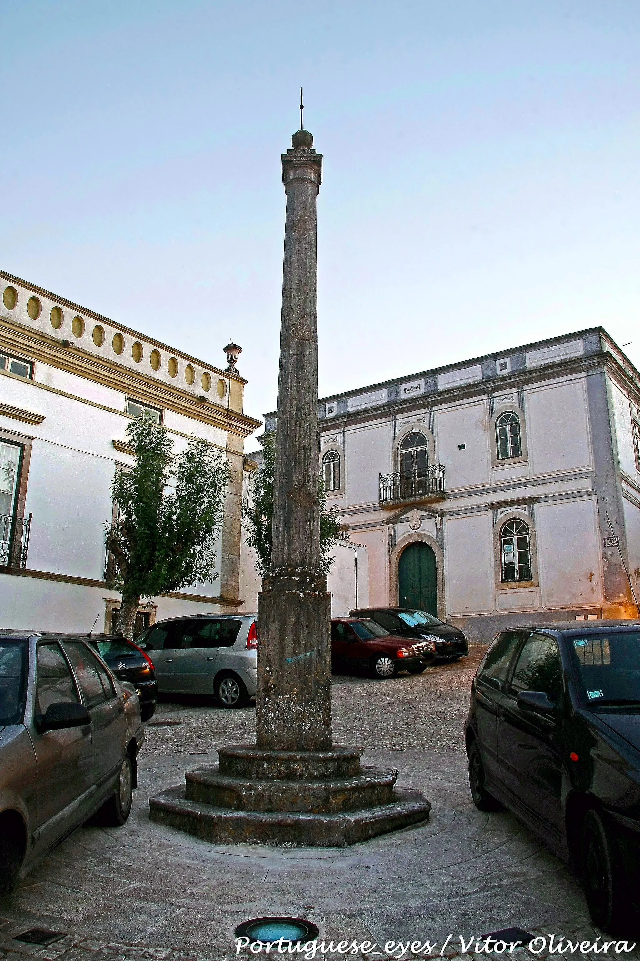 Photo showing: A localidade de Santiago do Cacém é de remotíssimas origens, conforme o comprova a proximidade das ruínas romana de Miróbriga, bem como de muitos vestígios de povoados neolíticos e das idades do cobre, bronze e ferro, e ainda de núcleos celtas. À ocupação romana (e à presumível fase visigótica) seguem-se cinco séculos de domínio árabe, desde o século VIII até ao século XII, que deixam importante marca na toponímia. Assim será a povoação conhecida por Vila do mouro Kassem, vila esta que constituiria o núcleo fortificado finalmente tomado pelos cavaleiros da Ordem de Santiago da Espada nos anos sessenta do século XII. Segue-se, em 1186, a doação de Kassem aos referidos Espatários, que a partir desta data, e particularmente após 1217 (vencida enfim a investida almôada que durante mais de trinta anos dominou a região, e confirmada por D. Afonso II a doação feita por seu pai à Ordem), ocuparam de facto o castelo e dinamizaram o povoamento do burgo, passando este a ser denominado por Terra (ou Castelo) de Santiago de Kassem. A importância da vila, assim considerada deste 1186, cresce de modo a receber a primeira carta de foral no reinado de D. Dinis, quando Santiago é temporariamente desanexada dos bens dos Espatários e doada a D. Vetácia Lascaris, aia da Rainha D. Isabel e preceptora da infanta D. Constança. Após a sua morte a vila regressou regressado à Ordem de Santiago, em cuja posse se manteve até 1594, quando Filipe II a doou aos Duques de Aveiro. O segundo foral de Santiago do Cacém é já manuelino, tendo sido outorgado em 1512. Embora seja de presumir o levantamento de um pelourinho em torno desta data, dele não restam vestígios, e o monumento actual é uma picota datada de 1845. 
Este pelourinho ergue-se na Praça Conde do Bracial, que constituía no século XIX o centro nevrálgico da vila. Encontra-se rodeado por várias casas nobres brasonadas, e pela Igreja da Misericórdia ou Igreja e Hospital do Espírito Santo, pelos antigos Paços do Concelho, e pela Torre do Relógio (em travessa que parte da praça). Trata-se de uma encomenda feita pela Câmara Municipal ao canteiro José Miguel Rodrigues, no ano de 1844, anterior ao da montagem na praça pública. 
Sobre um soco de três degraus octogonais assenta um paralelepípedo ao alto, e sobre este um plinto onde se pode ler a data mencionada, 1845. A coluna possui fuste de secção igualmente octogonal, estreitando em direcção ao topo, prolongado visualmente em capitel liso, com secção idêntica ao do fuste, entre duas molduras. O remate é composto por uma plataforma quadrada e saliente, encimado por um plinto quadrado e um globo, dividido em meridianos, assente em base cónica. O globo é por sua vez encimado por uma cruz evocativa da Ordem de Santiago, em ferro, com longa haste vertical. Possui algumas semelhanças com o Pelourinho de Palmela. SML www.igespar.pt/pt/patrimonio/pesquisa/geral/patrimonioimo...

See where this picture was taken. [?]