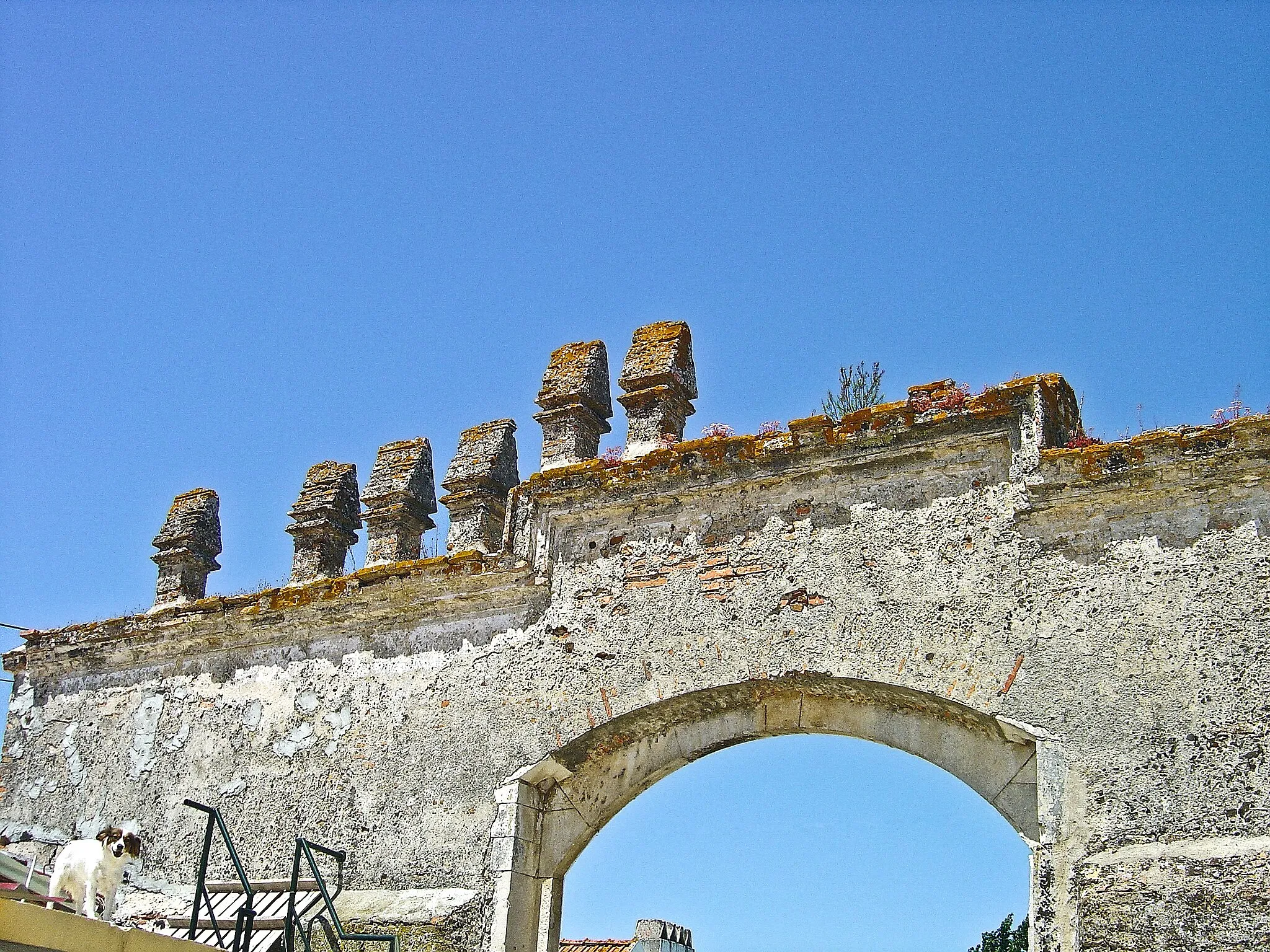 Photo showing: D. Manuel I no ano de 1512, mandou reconstruir um Paço na margem direita da Ribeira de Muge, um pouco a montante de Santo António da Raposa. O Paço era pequeno, não lhe faltavam porém comodidades. Era designado por Paço Real da Ribeira de Muge e servia de pousada aquando das caçadas e montarias da família real. Mais tarde, e como os servidores eram pretos (escravos) o Paço começou a ser designado por Paço dos Negros. Daí o nome da aldeia que cresceu a seu redor.
Possuia um pátio central composto por uma capela e residência real, cemitério, azenha, residência para servos, pomar, horta e manada de gado. Foi sede de almoxarifado.
Actualmente ainda se pode contemplar o pórtico, a capela, a azenha, a "planta" da traça original do paço e a cerca que circunda todo o complexo.
Zona arqueológica de importância crescente. Recentemente foi descoberta uma ponte romana da via Scalabis/Ebora. Toda esta zona, principalmente a que fazia parte do Paço Real da Ribeira de Muge, incluindo o pomar zona de pastagem de gado, está em processo de classificação de Interesse Municipal, pela impostância histórica e arqueológica que remontam até á época romana. pt.wikipedia.org/wiki/Pa%c3%a7o_dos_Negros

See where this picture was taken. [?]