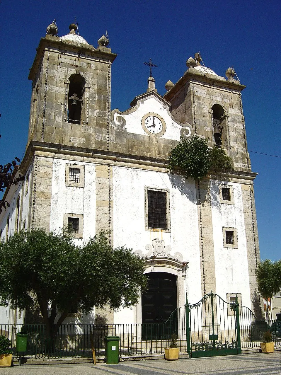 Photo showing: Em 1718, a Igreja existente em Samora Correia foi destruída, para dar lugar á actual Igreja Matriz, consagrada a Nossa Senhora de Oliveira, Padroeira da freguesia. A actual Igreja Matriz de Samora Correia, foi inaugurada e benzida em 1721, tendo sido mandada construir pelo Pároco Freire Henrique da Silva Araújo, da Ordem de Santiago da Espada. Para além de ser dedicada à padroeira, Nossa Senhora de Oliveira, consagra-se também, como monumento em honra do Apóstolo São Tiago Maior e da Ordem. A sua área coberta é de 650 m2 e o átrio vedado com gradeamento de ferro, é de 374,5 m2. Mede 14 metros, aos quais acrescentamos mais 6 metros da base das torres sineiras até ao pináculo. Os azulejos que revestem as suas paredes interiores, datam do século XVIII e fazem alusão ao Apóstolo São Tiago. Sobre um grande painel de jarras e florões de variada qualidade, desenham-se quadros da vida de São Tiago Maior, em dois maravilhosos e extensos painéis centrais, de 16 metros de comprimento por quase 2 de altura, ladeados de outros menores. A partir do século XII, São Tiago é apresentado como Apóstolo, pregando e ensinando, guerreiro geralmente a cavalo e com escudo, ou peregrino com manto, bordão, cabaça, largo chapéu e bolsa de couro presa à cintura. Só na Igreja de Samora Correia, ele aparece representado como peregrino-guerreiro, ao mesmo tempo, combatendo a pé, com hábito de peregrino e escudo de guerreiro. Os painéis estão simplesmente assinados por P.M.P.. Os terramotos de 1755 e 1909, provocaram vários danos, entre os quais o derrube de muitos azulejos, que depois foram colados à sorte e sem nexo, tendo portanto, ficado os painéis um pouco desfigurados. O altar-mor é em talha dourada, com a imagem da padroeira; do lado oposto ao da epístola, encontra-se um peque no retábulo com a imagem de Nossa Senhora do Ó. www.cm-benavente.pt/benavente/Concelho/LocaisInteresse/Pa...

See where this picture was taken. [?]