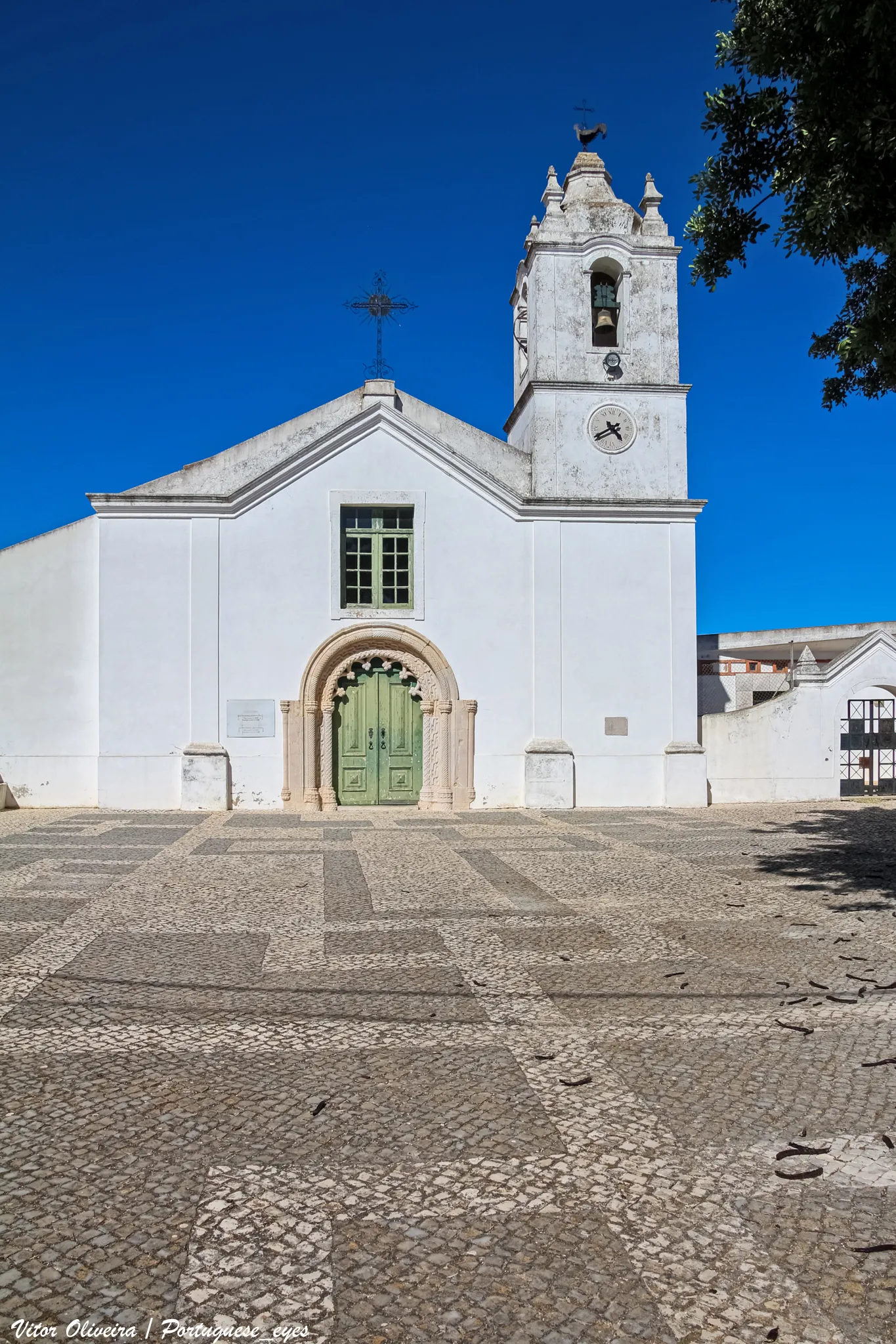 Photo showing: A Igreja Matriz de Odiáxere, também conhecida como Igreja de Odiáxere, é um edifício religioso localizado no concelho de Lagos, em Portugal.
Caracterização
Caracterização física
O edifício apresenta uma arquitectura predominantemente barroca, com um portal principal, de estilo manuelino, formando um arco pleno de intradorso, decorado por motivos entrelaçados; a bandeira do arco é totalmente ocupada por um cairel.
O corpo, de nave única, é de forma rectangular, com uma cabeceira quadrangular. Na parede de fundo, encontra-se um arco triunfal pleno, ladeado por dois altares, enquanto que a capela-mor, com um tecto de madeira formando um perfil de abóbada de berço, ostenta um retábulo em talha dourada, ladeado por colunas salomónicas.
Localização
A igreja localiza-se ao longo da Rua de São João e do Largo da Liberdade, no centro da localidade de Odiáxere.
Classificação e protecção
Este monumento encontra-se classificado como Imóvel de Interesse Público, segundo o Decreto n.º 2/96, DR n.º 56, de 6 de Março de 1996.
História

A igreja foi construída entre os séculos XV e XVI, tendo sofrido obras de ampliação e remodelação no interior em 1677, na mesma altura em que foi instalado o revestimento de azulejaria. Na primeira metade do Século XVIII foi construído o retábulo e alguns silhares de azulejos, e no Século XIX o edifício foi novamente modificado, tendo sido reconstruída a torre sineira, e alterada a a fachada. pt.wikipedia.org/wiki/Igreja_Matriz_de_Odi%C3%A1xere