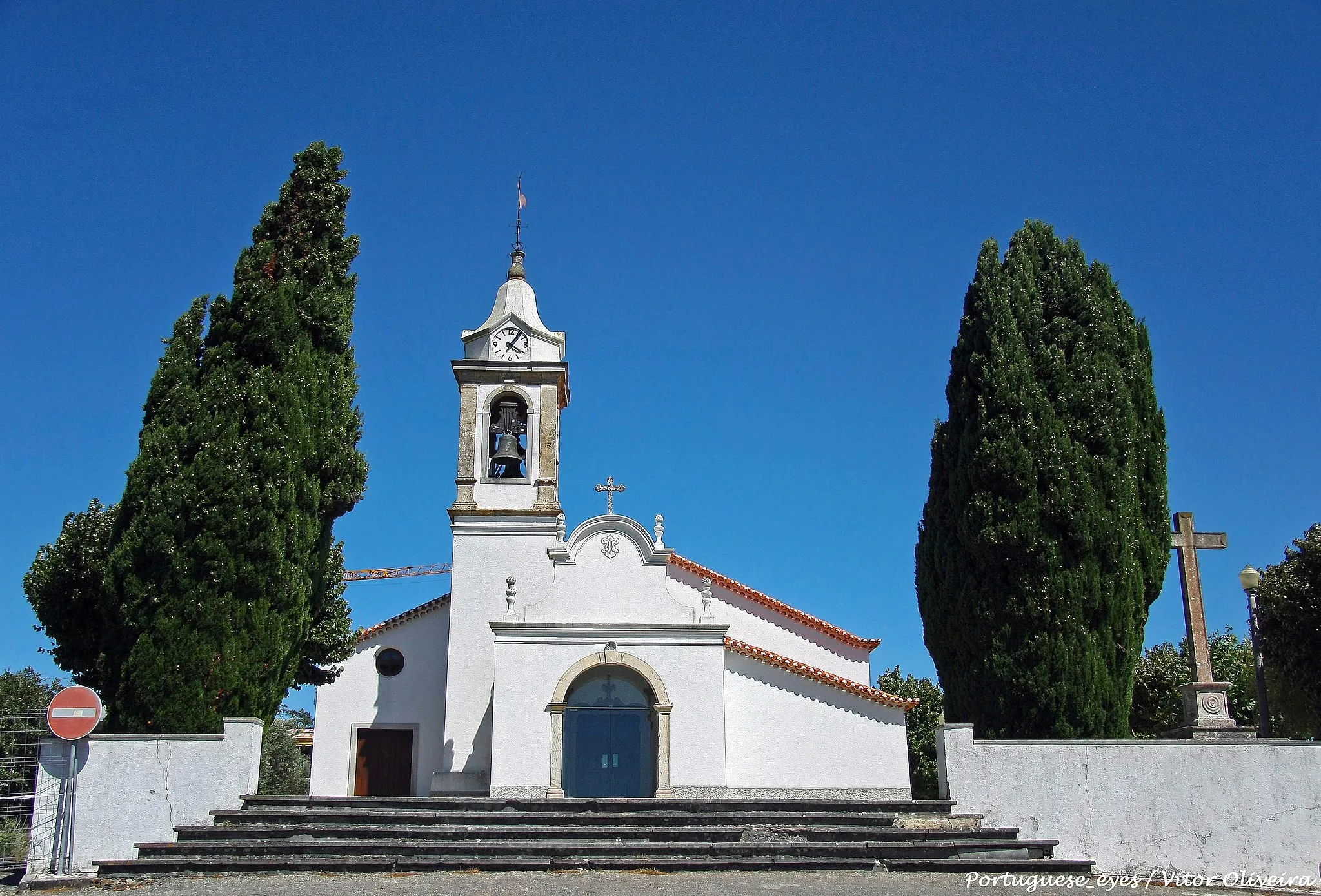 Photo showing: A igreja de São Miguel de Milharado é um dos muitos templos do concelho de Mafra que conserva elementos manuelinos, circunstância que lhe confere um lugar de destaque no processo de renovação (e de construção) de muitos monumentos religiosos durante a primeira metade do século XVI no nosso país. Nos séculos seguintes, foi objecto de várias reformas que contribuíram para enriquecer o conjunto monumental, alterando, quase por completo, a primitiva fisionomia quinhentista.
O mais importante vestígio é o portal principal, hoje inserido na galilé do templo. De duas arquivoltas, com ampla moldura interior entre elas, é de curvatura tripartida relativamente complexa, definida por dois arcos laterais a pleno centro, sem completar a volta inteira, que se ligam a um central, canopial, rematado por grinalda florida. Outras duas grinaldas partem da arquivolta exterior, coroando verticalmente o conjunto e conferindo-lhe um aspecto simétrico. As bases e os capitéis, de perfil oitavado, são bem marcados e a moldura interior é amplamente decorada com cestos e cachos de uvas, tendo por base as hastes de uma videira, sendo estas composições tuteladas axialmente pela figura de um anjo. Do período manuelino conserva-se ainda uma pia de água benta, de taça circular decorada com três bustos de anjos e assente em mísula cónica invertida, e um modilhão representando um busto humano, que originalmente estaria no exterior do edifício, mas cujas modificações posteriores fizeram com que integrasse a galeria de acesso à nave da igreja (VILAR, 2000, p.77).
A principal campanha reformadora aconteceu na viragem para o século XVII. De acordo com uma inscrição colocada sobre a porta de acesso ao púlpito, comprova-se que esta foi construída em 1609, ano aproximado de finalização do essencial das obras, partindo do princípio que o enriquecimento do interior terá tido lugar após a conclusão da renovação arquitectónica.
É no interior que se testemunham as principais obras Seiscentistas. De nave única, as suas paredes laterais são ritmadas por dois arcos de volta perfeita sobre pilastras, onde se incluem retábulos barrocos de talha dourada. Igual forma tem o arco triunfal, de desenvolvido embasamento e impostas e fecho axial bem vincados. O púlpito é circular, protegido com balaustrada de mármore, e a ele se acede através de uma porta de lintel recto. Estamos menos informados a respeito da reforma seiscentista do exterior, mas é de crer que a actual solução baixa da fachada principal, com corpo central em forma de galilé, aberto a poente por arco de volta perfeita, possa corresponder a esse período. Igualmente do século XVII é o cruzeiro do adro, sobre soco quadrangular de triplo degrau, com base cúbica decorada e cruz de arestas lisas sem decoração.
Nos séculos seguintes, as obras não cessaram no monumento, mas resumiram-se a trabalhos menores de arquitectura e a campanhas complementares de enriquecimento do interior. Sabemos que, em 1748, se revestiram as paredes da nave com azulejos, de padrão geométrico quadrangular. Em 1755, o mega-terramoto que assolou o centro e o Sul do país provocou o desabamento de uma casa de habitação anexa à igreja, que servia de apoio a peregrinos, mas não danificou grandemente o templo, pois nenhuma obra é mencionada em 1760, ano em que um visitador determina apenas a reconstrução da albergaria. Por essa mesma altura devem ter-se realizado os retábulos de talha dourada, uma vez que alguns apresentam já características rococós, e é possível que a quadrangular torre sineira, que coroa a galilé da frontaria, date deste mesmo século XVIII, ainda que o seu coroamento nos pareça já posterior.
Restaurada integralmente em 1960, a paroquial de São Miguel espelha bem a evolução artística das construções religiosas da região rural a Norte de Lisboa que, partindo muitas vezes de um pequeno templo tardo-medieval, passaram a sede de paróquia e foram, por isso, alvo de numerosos melhoramentos nos séculos XVII e XVIII.
PAF

www.patrimoniocultural.gov.pt/en/patrimonio/patrimonio-im...