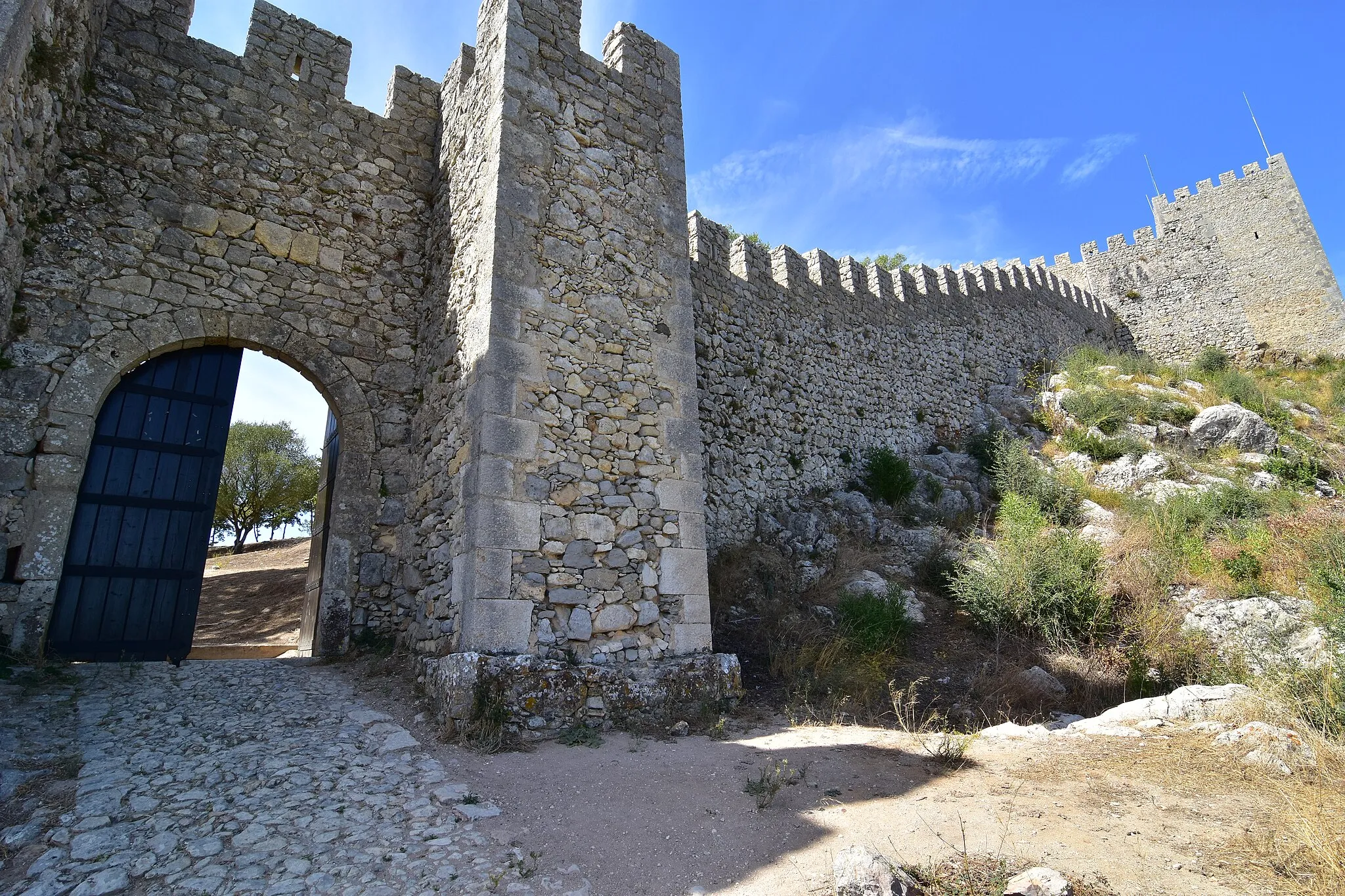 Photo showing: Sesimbra Castle, main entrance viewed from outside the walls. The keep can be seen at the right.

Entrada do castelo, vista do lado de fora das muralhas. A torre de menagem pode ser vista a direita.