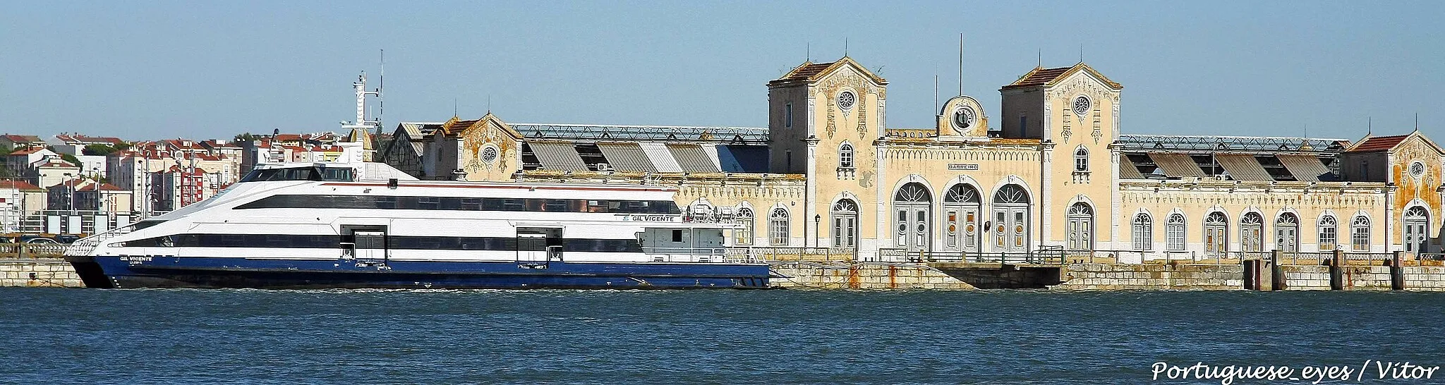 Photo showing: Foi uma das mais imponentes estações da margem sul, e chegou a ter tanta gente a circular diariamente, que foi construído um pequeno centro comercial para aproveitar as enchentes que se repetiam em horas de ponta. A sua localização sempre permitiu que se tornasse um cartão de visita para quem chega ao Barreiro vindo pelo Tejo. Hoje não passa de um imóvel fantasma onde o silêncio só é interrompido pelo vento a bater nas poucas telhas que ainda restam da sua cobertura, quando este existe.
Construída há mais de 130 anos, a Estação Ferroviária do Barreiro, inicialmente designada por Estação do Caminho de Ferro do Sul e Sueste, e popularmente conhecida por Estação do Barreiro-Mar, foi um projecto da autoria do Engenheiro Miguel Pais, e visava resolver a distância que existia entre a anterior estação e o cais dos barcos e assim aproximar o mais possível as duas margens do Tejo. Esteve activa durante 124 anos, desde 1884 até 2008, aquando da nova construção, uns míseros metros ao lado, da nova estação do Barreiro que estava inserida no plano de "modernização" da linha do sado. A estação de Setúbal, que também pertence à linha do Sado, viu a sua antiga estação ser inserida na nova, preservando toda a beleza e traçado da antiga arquitetura visível no exterior do edifício. Já a estação do Barreiro não teve essa sorte. Foi totalmente abandonada (pelo menos na sua principal serventia, como estação) para ser construído ao lado um conjunto de blocos de mármore rosado, uns painéis de vidro e umas estruturas metálicas de cor negra. Tem a sua beleza, modernamente falando. 
Na altura da desativação da antiga estação ouviu-se por aí, com pompa e circunstância, que era do profundo interesse da autarquia Barreirense preservar a antiga estação, pois estávamos a falar de um ícone Barreirense tal como os abandonados moinhos de água de Alburrica, o abandonado palácio de Coimbra, o abandonado posto médico da CUF, a abandonada Torre do Inferno em Coina, e outros tantos abandonados edifícios e monumentos que fazem parte da história barreirense.
Politicamente falando, ainda devem estar a ser estudados projectos para requalificação da estação assim como o seu espaço adjacente, mesmo já tendo passado quase 10 anos desde a sua desativação como estação. Vejamos o lado positivo, acaba por estar agora mais fácil de substituir as antigas telhas da estação, visto que grande parte das mesma já caíram, ou voaram com o vento. Esperemos é que não se descubra entretanto que são feitas de amianto, se não estamos mais 10 anos a "estudar projectos" para a sua remoção.
Antes de se chegar à estação, passamos por um conjunto de rotundas e obstáculos feitos de carros. Uma via onde a lei do lugar é criada por quem chegar primeiro. Mais parece uma feira de usados, mas tudo usados de grande categoria! A julgar pelas bombas que se vêem lá, até custa a crer que o dono de um Porsche 911 se tenha esquecido da carteira em casa e não possa pagar o euro e vinte de parque pago do outro lado da linha, perto da estação dos barcos. Mas esquecimentos acontecem, e as carteiras são as que mais sofrem, por serem esquecidas em casa como é óbvio.
Quer queiramos quer não, estaríamos a falar de valores muito altos pois a requalificação do edifício e espaço à volta exigia entre muitos outros aspectos, um exaustivo trabalho de profissionais qualificados para a obra. Por outras palavras, "é muita complicado!". 
Mas há solução! Venda-se a quinta Braamcamp! Estava a brincar... Também tem a sua história e ainda bem que a câmara a comprou, assim evita-se que seja destruída. Felizmente já quase não há lá nada para destruir.
Resumindo e concluindo, já era tempo do Barreiro olhar para trás e fazer uma "vénia" a todas as coisas, e não só a algumas, que a transformaram ou ajudaram a transformar-se na grande Cidade que é hoje, com todos os seus defeitos e virtudes, como todas as terras neste país. É importante inovar e evoluir, mas sem nunca esquecer quem nos ensinou.
João Naia da Silva

www.rostos.pt/inicio2.asp?cronica=11000371