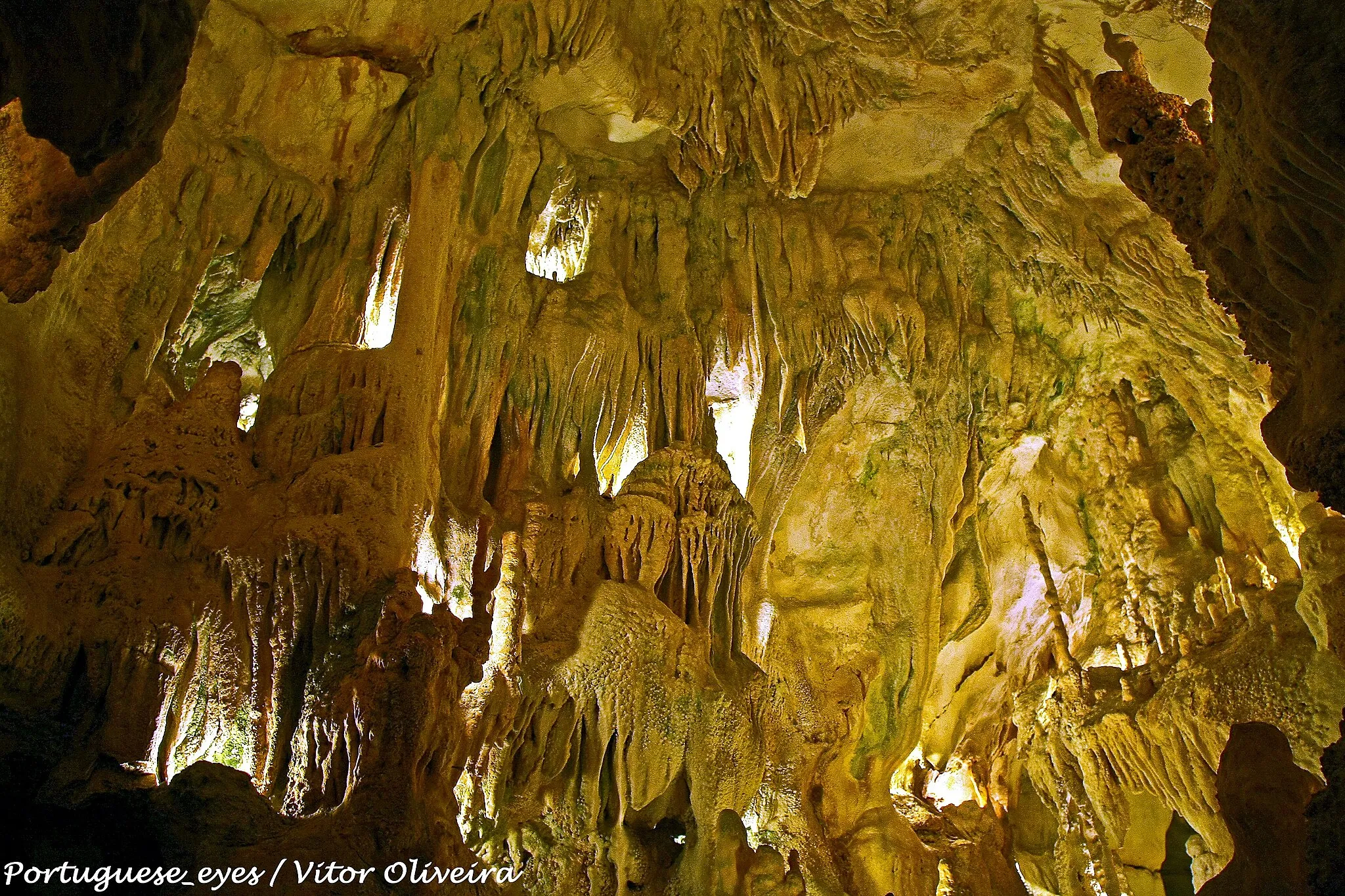 Photo showing: As grutas foram descobertas em 1971 por dois caçadores que andavam a perseguir uma raposa. A curiosidade levou-os a explorar o algar em toda a sua extensão, logo uma sala - a "Sala do Pastor", repleta de formações calcáreas. Durante perto de dois meses, os dois homens continuaram a escavar as estreitas fendas que se seguiram à primeira caverna, desvendando pouco a pouco as demais salas e galerias que hoje se incluem no percurso visitável.
Entretanto foram contratados geólogos e outros técnicos e procedeu-se ao aproveitamento da gruta como atração turística preservando-se rigorosamente as suas características incluindo a paisagem serrana da superfície.
Características
A beleza da gruta é assegurada pela diversidade de materiais argilosos e de calcites. Os nomes das salas sugerem as imagens que cada uma evoca ao visitante: "Presépio", "Pastor", "Cascata", "Virgem", "Cúpula Vermelha", "Marítima", "Capela Imperfeita", "Bolo de Noiva", "Abóbada Vermelha" e "Fonte das Lágrimas".
A extensão visitável da gruta é de 350 metros, atingindo-se uma profundidade de 45 metros. A temperatuira interior da gruta é, em média, de 18 graus Celsius.
A entrada e saída da gruta é feita em locais diferentes, envolvidos por uma característica paisagem serrana.
Lenda da Gruta
Segundo a tradição local, um homem abastado das redondezas, ao passar por um matagal em torno de um covão, foi atacado e saqueado por um bando de malfeitores que o assassinaram, como era frequente em tempos idos. O corpo sem vida foi atirado para o precipício cavernoso e, na pressa, os assaltantes deixaram cair, com o corpo da vítima, o saco das moedas que esta transportava e cujo roubo fora o móvel do crime. As moedas se espalharam pelo precipício, perdendo-se irremediávelmente, o que deu ao algar o nome pelo qual ainda hoje é conhecido. pt.wikipedia.org/wiki/Grutas_da_Moeda

See where this picture was taken. [?]