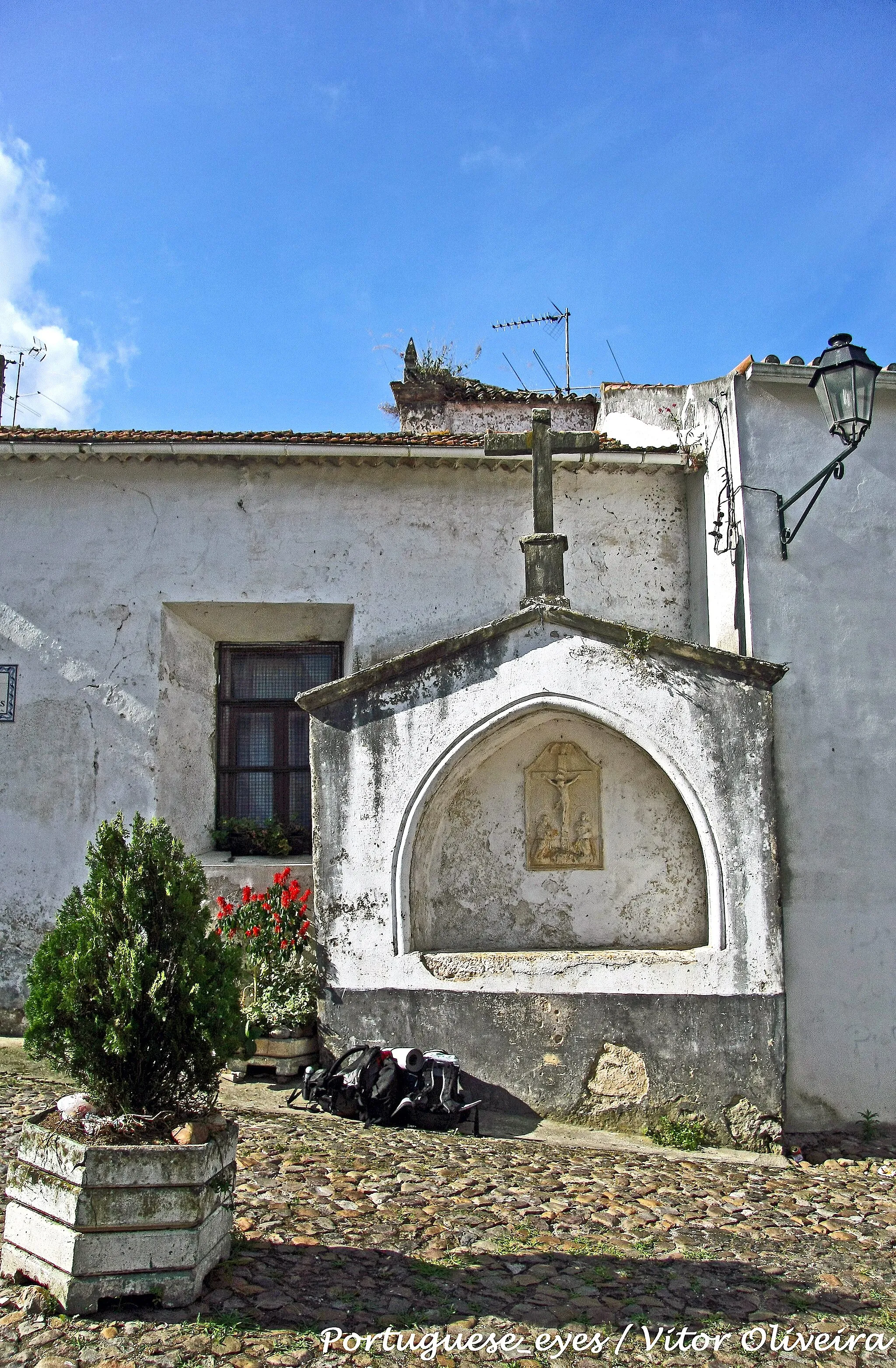 Photo showing: Situado no velho burgo de Celas, em Coimbra, o cisterciense Mosteiro de Sta. Maria de Celas foi fundado por D. Sancha, filha de D. Sancho I, por volta do ano de 1213. O seu magnífico claustro mostra obra de várias épocas. A atual disposição data do século XVI, mas o grande destaque vai para as alas sul e poente, obra do século XIV formada por 12 arcos plenos, assentes em esbeltas colunas geminadas, contendo extraordinários capitéis historiados de temas cristológicos e hagiográficos, a par com uma decoração de quimeras e motivos fitomórficos.
A infanta mandou construir uma igreja com um pequeno claustro e à sua volta diminutas celas. A evolução da comunidade religiosa andou a par com a expansão das dependências conventuais, conhecendo estas vários períodos de restauro, especialmente nos séculos XVI e XVIII. Extintas as ordens religiosas em 1834, foi permitido às monjas bernardas a sua continuação, até à morte da última, que ocorreu em finais do século XIX.
A fachada do Mosteiro de Celas é rasgada por um portal nobre quinhentista, de vão retangular enquadrado por pilastras com terminações pinaculares. As pilastras são rematadas por saliente cornija sobrepujada por frontão triangular. No lado direito abre-se um outro portal manuelino, de menores dimensões, encimado por janela polilobada. O piso superior é marcado por galeria seiscentista coberta e rasgada por nove vãos gradeados. À direita ficava a casa da abadessa (hoje escola primária), a cozinha e o refeitório; à esquerda, podemos ver as ruínas das antigas hospedarias, do cartório conventual do século XVII e, ao fundo, um portão.
Antecedida por um pequeno átrio, a igreja de planta circular, da autoria de Gaspar Fernandes e João Português, foi acabada em 1529. A capela-mor fica à direita da entrada, em linha oposta ao coro. Cobre a igreja uma belíssima abóbada manuelina estrelada, com nervuras calcárias ornamentadas por chaves de florões, ostentado a do fecho o escudo português segurado por duas águias. É de salientar o lambrim de azulejos, da segunda metade do século XVIII e de fabrico coimbrão, versando cenas da Anunciação e da Visitação. Ladeiam o arco cruzeiro dois altares, o da Piedade e o de Cristo. Nas paredes aparecem alguns quadros, com destaque para a magnífica Anunciação quinhentista e a Coroação de Maria, Santa Isabel e "Ecce Homo", do século XVII.A ousia setecentista apresenta grande arco com as armas de Portugal e de Cister. O altar-mor, de madeira dourada e marmoreado, ostenta esculturas da mesma época, de S. Bento e de S. Bernardo, e uma pintura de N. Sra. com o Menino. Na sacristia encontra-se a predela de um retábulo em pedra, com baixo-relevo de S. Martinho, com toda a probabilidade uma das obras que a abadessa encomendou no século XVI a João de Ruão.O arco do coro, setecentista, apresenta uma pequena abóbada manuelina com as armas dos Vasconcelos. Preenche o arco um interessante gradeamento em ferro forjado, saído da oficina de Coimbra do século XVIII. O coro, simples e espaçoso, ostenta um cadeiral de duas filas com alto espaldar, obra de finais do século XVI, de Gaspar Coelho.
A porta do coro para a antecâmara da sala do cabido deve-se a Nicolau Chanterene e ostenta a data de 1526, mostrando as armas da abadessa D. Leonor de Vasconcelos e de D. Sancha.A sala do capítulo apresenta cobertura de pedra em abóbada de caixotões, revestindo as paredes azulejos seiscentistas sobre os pétreos bancos corridos. No arco do topo assenta em mísula a escultura de Cristo Ressuscitado, abrindo-se dos lados nichos albergando S. Bento e S. Bernardo.
O magnífico claustro do mosteiro mostra obra de várias épocas. A atual disposição data do século XVI. A galeria norte e nascente, do século XVI, desenvolve-se em três grupos de dois arcos, apoiados em colunas dóricas. As alas sul e poente pertencem ao século XIV e são formadas por 12 arcos plenos, assentes em esbeltas colunas geminadas, com extraordinários capitéis historiados com temas cristológicos e hagiográficos, a par com uma decoração de quimeras e motivos fitomórficos.
No Museu Nacional de Machado de Castro, em Coimbra, encontram-se algumas peças que foram pertença do mosteiro. É o caso do baixo-relevo da Paixão, atribuído a João de Ruão; de um grande crucifixo em pedra; dois capitéis, representando um o Pentecostes e o outro Cristo em Majestade; e de seis pinturas manuelinas que integravam o antigo retábulo-mor, atribuídas à quinhentista oficina de Coimbra constituída pela dupla Vicente Gil e Manuel Vicente. In Infopédia [Em linha]. Porto: Porto Editora, 2003-2013. [Consult. 2013-03-18]. www.infopedia.pt/$convento-de-celas

See where this picture was taken. [?]