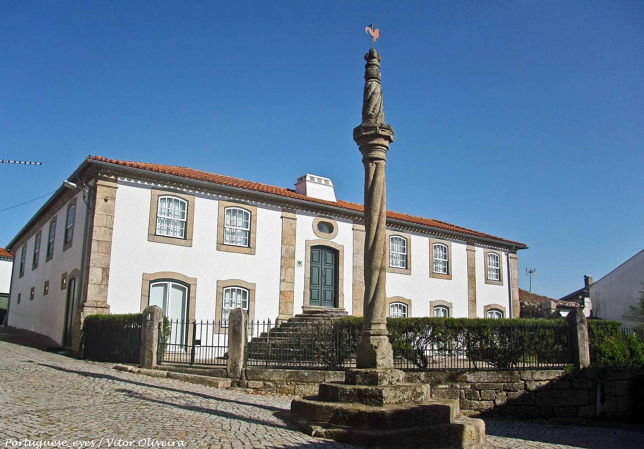 Photo showing: Estrutura em cantaria de granito, composta por soco de quatro degraus escalonados, com base paralelepipédica quadrangular de vértices chanfrados superiormente. Plinto circular com toro, onde assenta fuste torso de quatro vergas espiraladas encimado por gola côncava entre molduras. Ábaco saliente, oitavado, com anel circular, remate cónico, torso, de dois registos escalonados, separados por gola estreita, finalizando em pequeno coruchéu de cinco esferas sobre anel. Sobre a esfera superior um galo catavento. A um terço da altura do fuste, dois furos tapados com gesso, indicam onde estiveram cravados os ferros de sujeição. www.monumentos.gov.pt/Site/APP_PagesUser/SIPA.aspx?id=2558