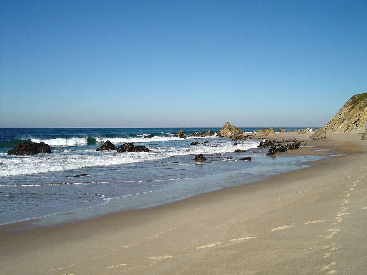 Photo showing: Para descobrir a origem do nome desta praia não é preciso triturar os neurónios, não senhor. E a chave para aturar este tipo de desafios está em ter uma paciência de santo…
Pois bem, pode não parecer, mas as pistas para descobrir o nome do lugar onde foi tirada esta foto estão todas no parágrafo acima! 
Boa sorte.

See where this picture was taken. [?]