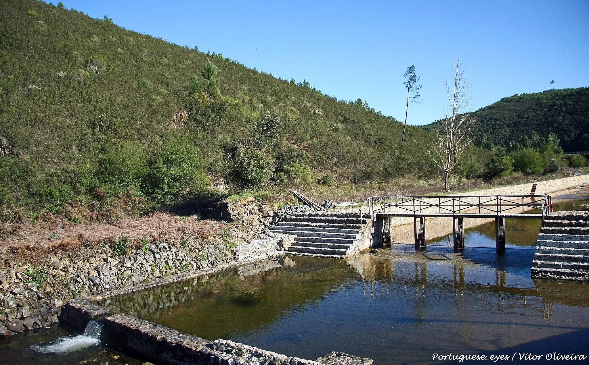 Photo showing: Situada na fronteira entre a freguesia de Fundada e São João do Peso, esta praia é uma das mais recentes alternativas do concelho de Vila de Rei para fugir ao intenso calor dos meses de Verão. Rodeada por montes ricos em biodiversidade e onde quase não se nota a presença humana, a zona balnear de Bostelim tem o sossego e a proximidade à natureza como nota dominante.
Como já vem dando sinais, desde que foi inaugurado em 2007, o espaço fluvial promete transformar-se num dos destinos preferidos dos banhistas, no concelho de Vila de Rei. O espaço acolhe, também, o Parque de Campismo Rural do Bostelim, onde tem início o percurso pedestre Rota do Bostelim de 9km, entre levadas, açudes, moinhos e uma ponte centenária.

A zona reservada a banhos é de excelência, especialmente para programas em família, sendo bastante seguro para as crianças e pessoas que requeiram maiores cuidados. Também a área contígua à linha de água é dotada de sombras naturais e solo relvado, para o maior conforto dos utentes. aldeiasdoxisto.pt/poi/4052