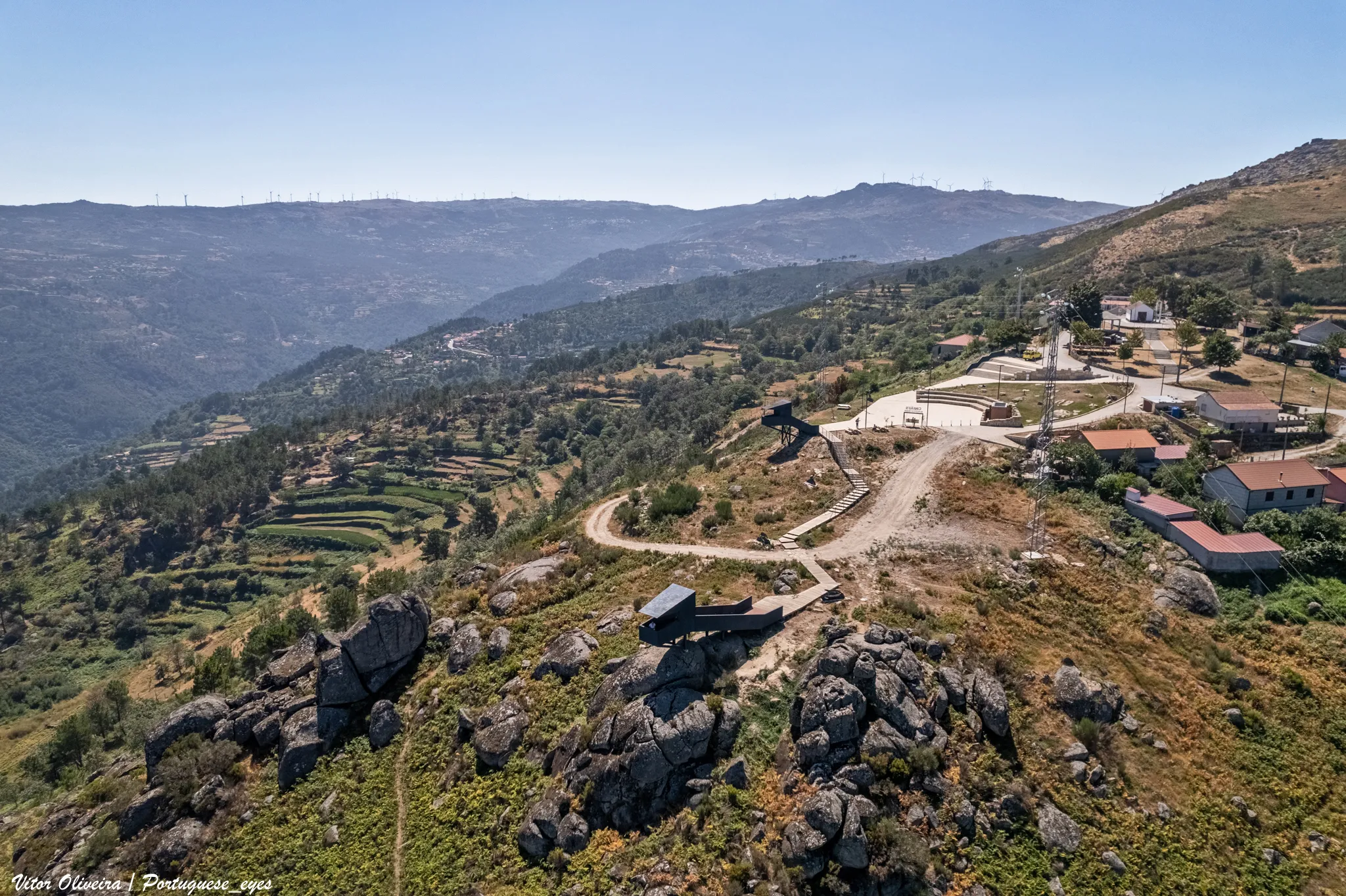 Photo showing: Situado em plena Serra do Montemuro, o projeto contempla uma paisagem caracteristicamente composta por mosaicos, tais como aglomerados rurais, agricultura e floresta, capazes de albergar uma diversidade faunística e florística imensa. Mais concretamente localiza-se no espaço adjacente à Rua do Miradouro, na localidade de Marcelim, pertencente ao concelho de Cinfães, num troço próximo da Capela de Nossa Senhora dos Milagres. O projeto consiste na construção de dois pontos de observação estrategicamente colocados, um no patamar superior, com vistas orientadas para o vale do rio Bestança, e outro no patamar inferior, com vistas orientadas para a foz do rio Bestança e o vale do rio Douro. A presente operação visa atribuir uma nova funcionalidade ao espaço como espaço público de lazer, tirando o melhor proveito das mais-valias e vistas que esta área proporciona, tendo em conta as suas características naturais, de compatibilização com as mesmas e numa perspetiva de sustentabilidade, indo assim ao encontro dos objetivos do eixo prioritário de investimento, que se baseiam na conservação, proteção, promoção e desenvolvimento do património natural e cultural. Com a implementação da intervenção proposta, o município de Cinfães pretende alavancar o investimento no Turismo de Natureza, sendo este considerado como um dos principais produtos turísticos prioritários da Região do Norte, como emanado na Agenda Regional do Turismo. O projeto tem como objetivo a criação de um espaço de visita e lazer, permitindo a valorização dos recursos naturais existentes no Município, com equipamentos e infraestruturas de apoio ao seu funcionamento, nomeadamente, pavimentações, zona de estacionamento, espaço pedonal e zonas com mobiliário urbano. É também pretendida a criação de plataformas, tipo observatórios da natureza, para que os visitantes possam usufruir da paisagem do local. A operação visa também a aposta num turismo acessível para todos, promovendo a acessibilidade a pessoas com deficiência ou incapacidade. Neste sentido o projeto prevê a colocação de um elevador para pessoas com mobilidade reduzida, tornando possível o acesso da parte superior por pessoas em cadeira de rodas ou com dificuldade de locomoção. A proposta tem como premissa a requalificação do espaço a intervencionar, tornando-o um local de usufruto público dedicado ao lazer e à fruição da paisagem, tendo como base a incomparável potencialidade das vistas que esta zona proporciona, permitindo assim alcançar um objetivo primordial que se traduz no aumento do número de visitantes a sítios de património cultural e natural. Pretende-se que o Observatório da Natureza de Marcelim constitua uma mais-valia como espaço público para todo o concelho e a região Norte do país, constituindo-se como um espaço utilizável por todos os visitantes e tornando-se num ponto atrativo para o Turismo de Natureza. Desta forma, o município visa promover o equilíbrio necessário entre o desenvolvimento, o investimento e o respeito pela biodiversidade e conservação da natureza, adotando e concretizando políticas e ações que visam o Turismo Sustentável. cm-cinfaes.pt/acao-municipal/portugal-2020-mm/item/3662-o...