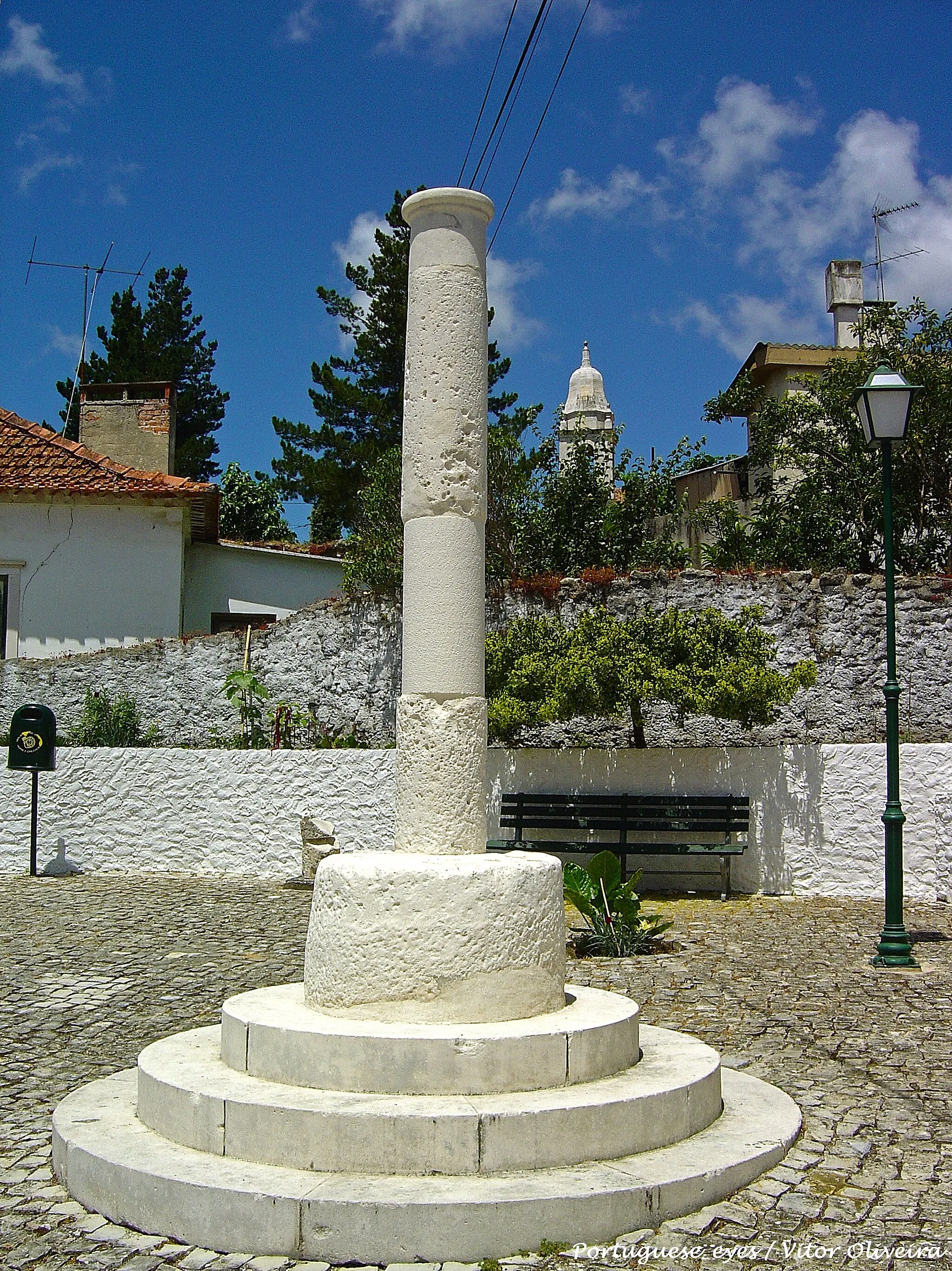 Photo showing: A povoação de Alpedriz foi conquistada ao domínio árabe por D. Afonso Henriques, em 1147. Recebeu o seu primeiro foral em 1150, das mãos do mesmo rei, que assim incentivava o seu povoamento. Em 1187, D. Sancho I entrega a vila como comenda aos freires da Ordem de São Bento de Avis. D. Manuel concedeu-lhe foral novo, em 1515.

A actual freguesia, integrada em Alcobaça desde o século XIX, possui um monumento geralmente designado como Pelourinho de Alpedriz, num largo central da povoação, junto à Ermida do Santíssimo Sacramento. A sua datação é incerta, para o que contribui a simplicidade dos elementos que restam: do original, existe apenas o fuste, este mesmo bastante intervencionado. Este fuste esteve levantado em posição distinta no mesmo largo, sobre uma base tronco-cónica alta e lisa. Foi derrubado em 1973, e reerguido sobre um soco de três degraus circulares, feitos de novo (mantendo a base). O fuste, que até então apresentava um forte adelgaçamento na metade inferior, aparentemente causado por desgaste (?), foi corrigido com cimento. Veio a ser novamente deitado por terra em 1992, e desta vez a sua reconstrução, a cargo da Junta de Freguesia de Alpedriz e efectuada em 1994, incluiu a feitura de uma base nova para a coluna, em substituição do anterior tronco de cone. A plataforma é igualmente distinta, bem como o remate, até então inexistente. Assim, e ao presente, o pelourinho é constituído por um soco de dois degraus quadrangulares, de parapeito boleado, aparentemente antigos (?), sobre os quais assenta a base da coluna, desta feita constando de um grande paralelepípedo liso. Sobre este levanta-se directamente o fuste, cilíndrico e ligeiramente galbado, revestido com cimento. Termina com uma estreita moldura circular, e é rematado por uma cruz de época distinta do fuste. Está, pois, transformado em cruzeiro, fazendo conjunto com a ermida já citada. Note-se a intenção de fazer concordar a planta da base, feita de novo, com a dos degraus, possivelmente aproveitados de outro monumento. SML www.patrimoniocultural.pt/pt/patrimonio/patrimonio-imovel...