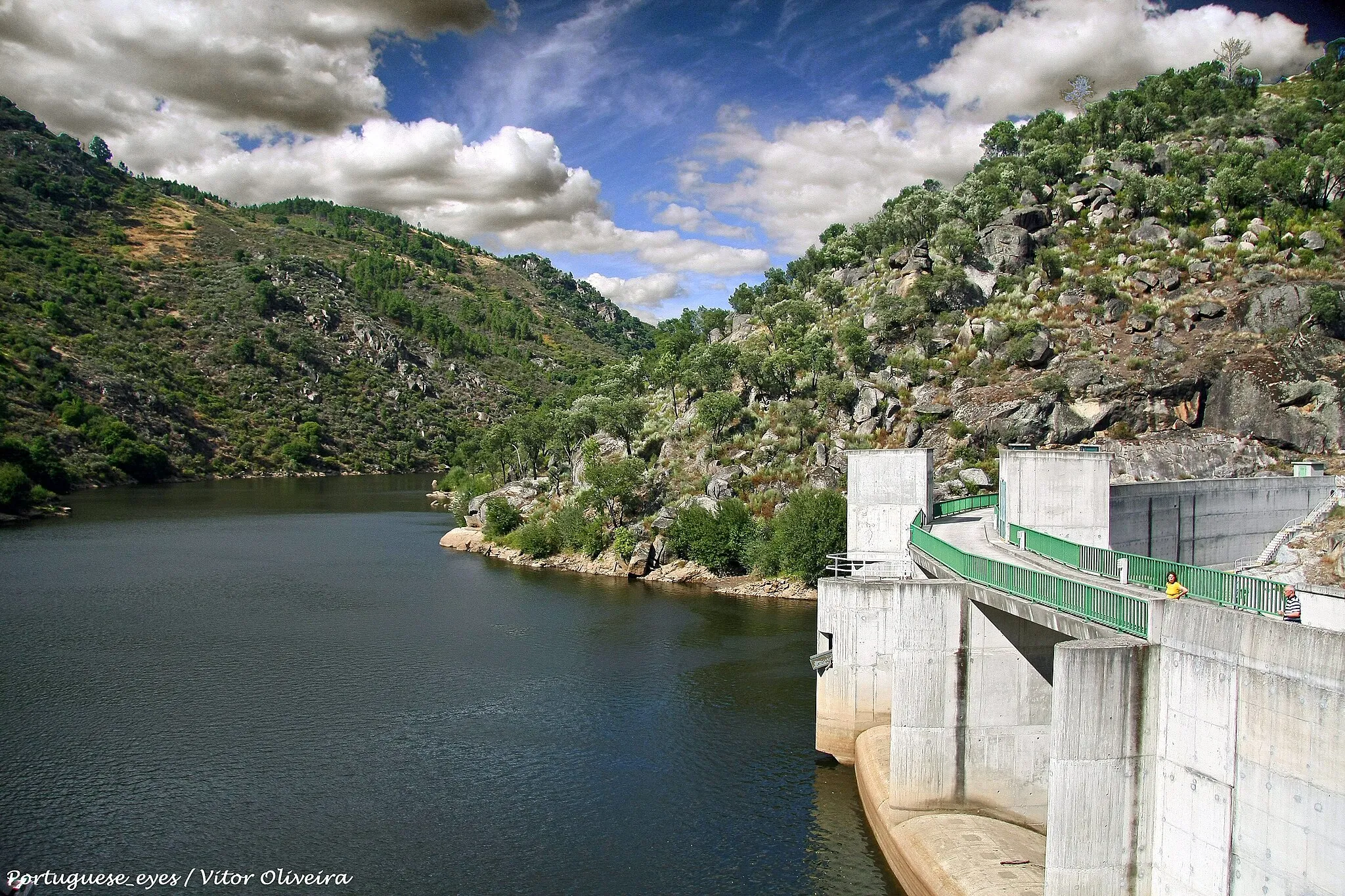 Photo showing: A barragem de Rebordelo localiza-se no concelho de Vinhais, distrito de Bragança, Portugal. Situa-se no rio Rabaçal. A barragem foi projectada em 1999 e entrou em funcionamento em 2004.
Barragem
É uma barragem de arco e gravidade em betão. Possui uma altura de 35,5 m acima da fundação e um comprimento de coroamento de 127 m. O volume de betão é de 19.000 m³. Possui uma capacidade de descarga máxima de 1.480 m³/s.
Albufeira
A albufeira da barragem apresenta uma superfície inundável ao NPA (Nível Pleno de Armazenamento) de 46 hectares e tem uma capacidade total de 3,13 hm³. As cotas de água na albufeira são: NPA de 380 metros, NMC (Nível Máximo de Cheia) de 386 metros e NME (Nível Mínimo de Exploração) de 378,5 metros.
Central hidroeléctrica

A central hidroeléctrica é constituída por um grupo Kaplan com uma potência instalada de 8,75 MW. A energia produzida em média por ano é de 24 GWh. pt.wikipedia.org/wiki/Barragem_de_Rebordelo