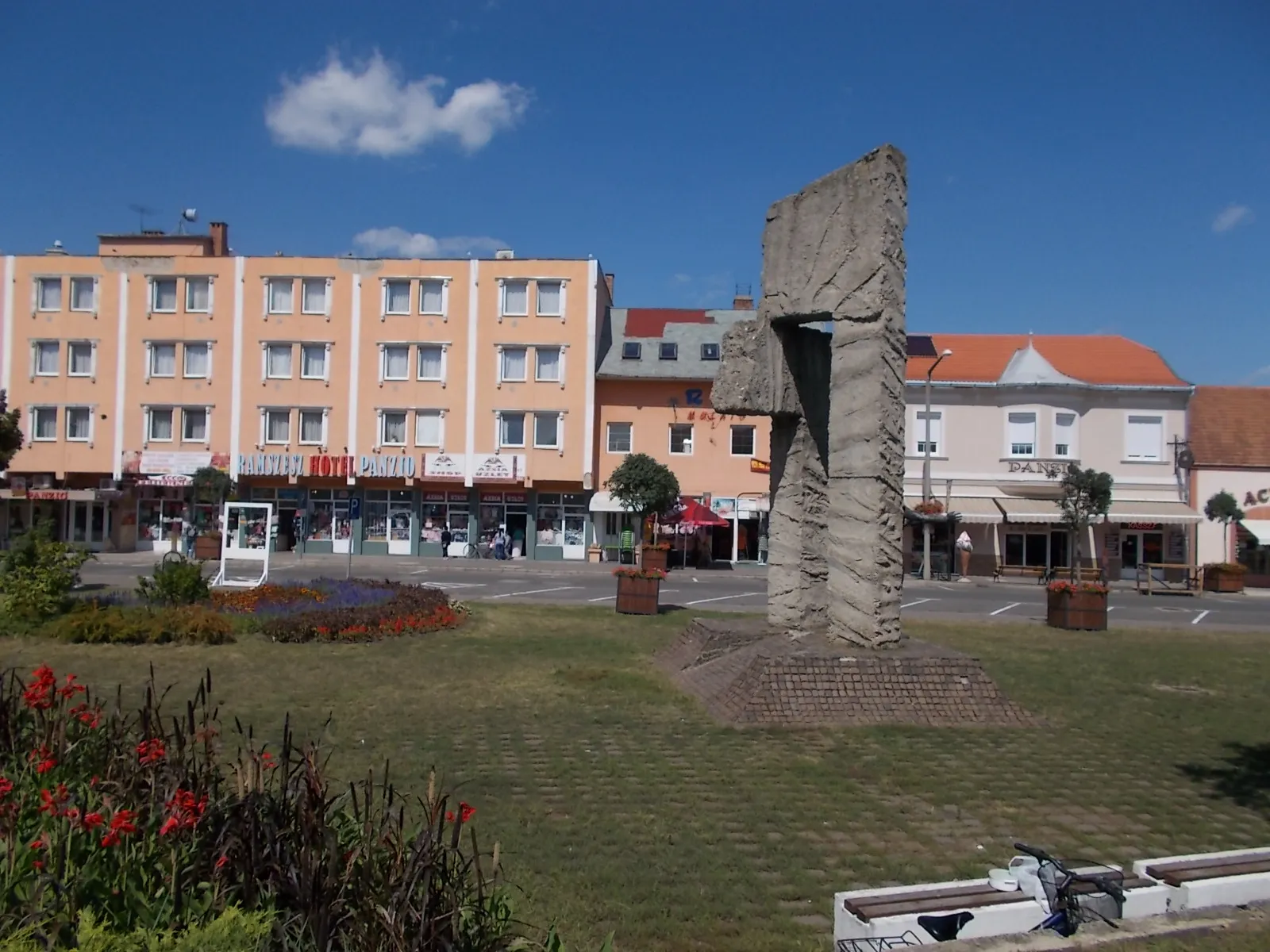 Photo showing: Freedom memorial by István Kiss, (1981, concrete gate is 8 meters high and 3 meters wide, two and a half meters high male with flowers in his hand stand on a basalt cube pile, a replacement of the WWII memorial?, planned in 1975, a simple agricultural worker figure who enjoying the Life, and the liberation) - Hősök Square, Mátészalka, Szabolcs-Szatmár-Bereg County, Hungary.