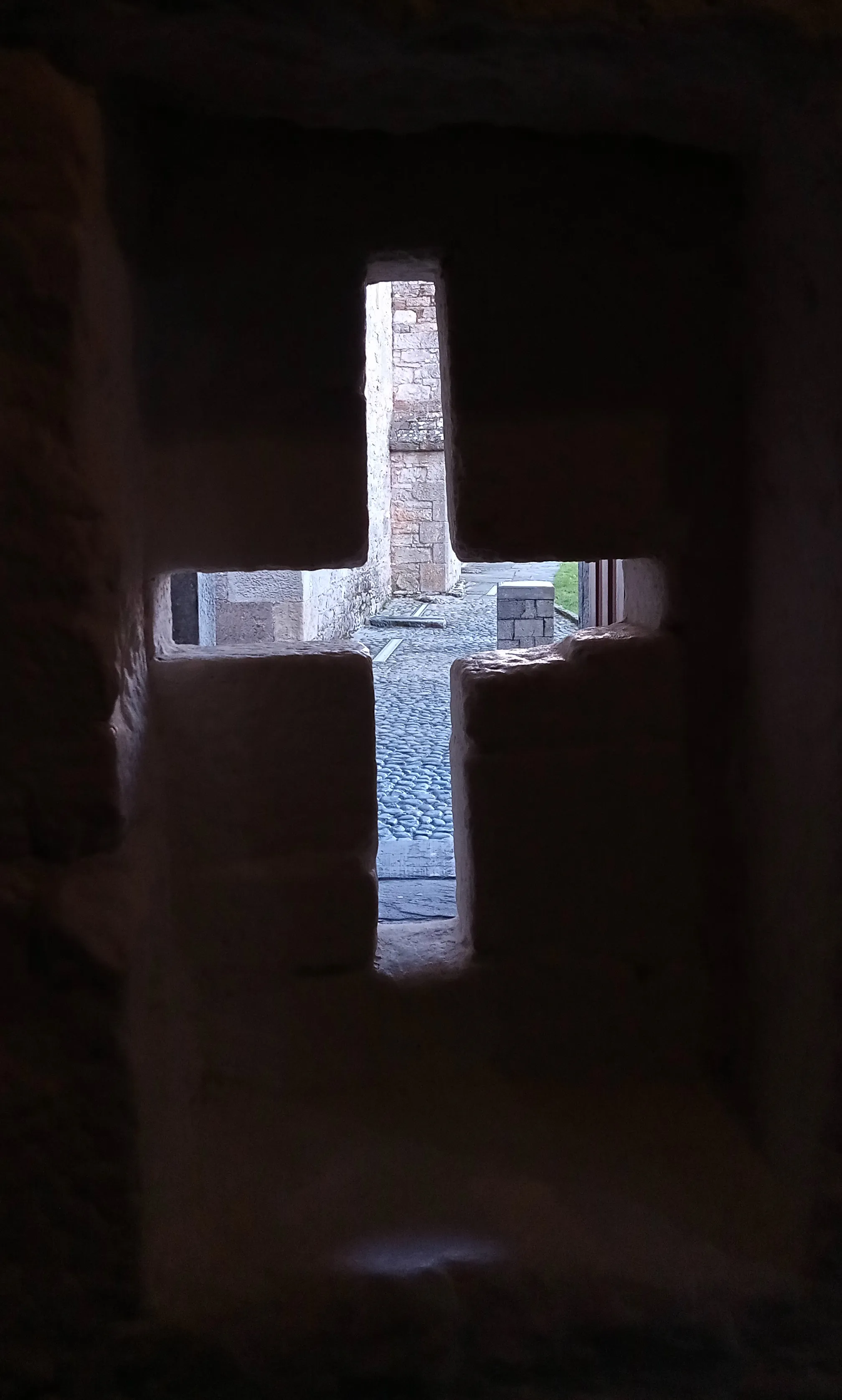 Photo showing: The cross-shaped loophole at Cahir Castle from inside. A knee rest is visible in the dark below, and you get an idea of the range and view the shooter had.