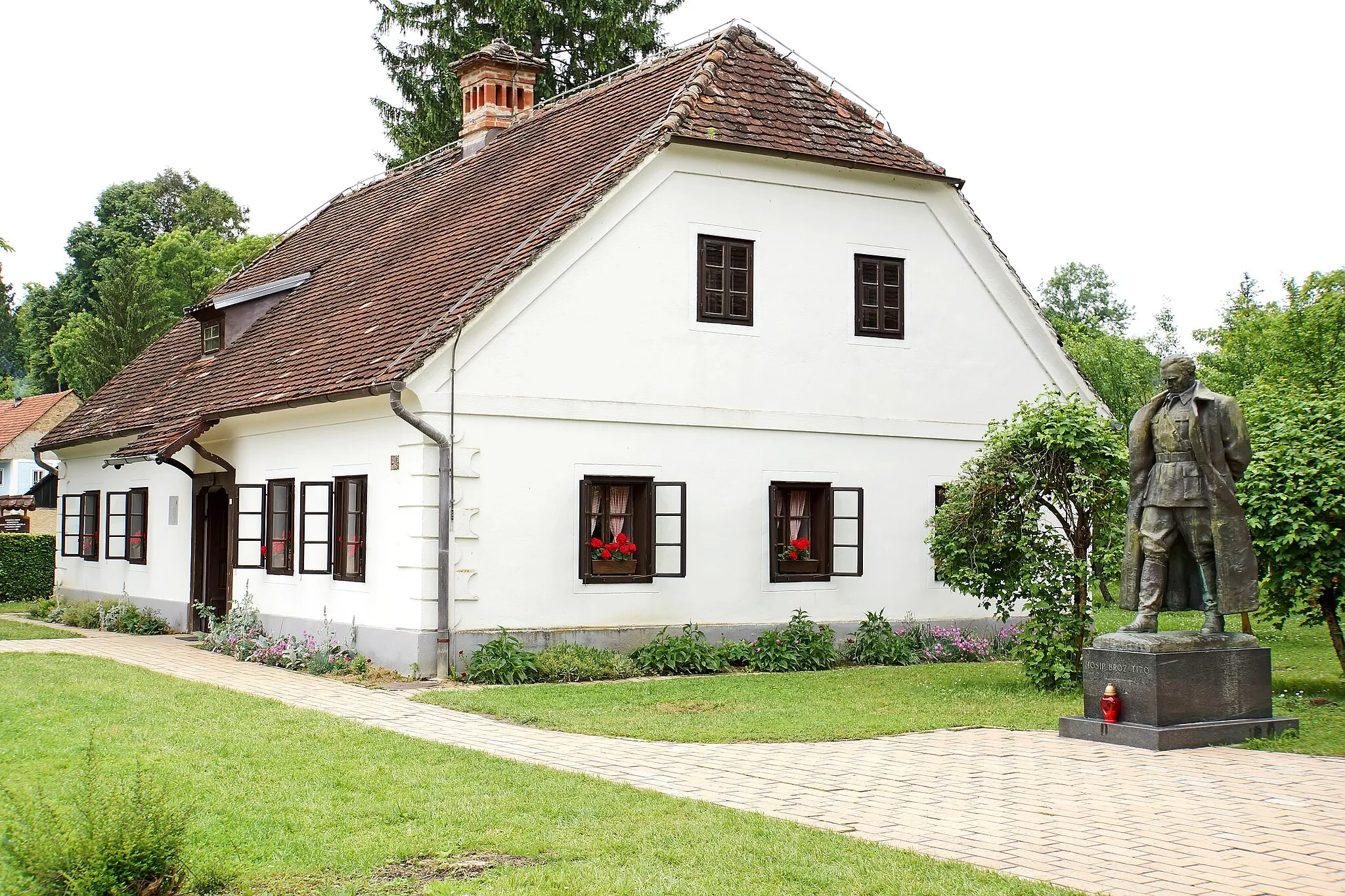 Photo showing: Kumrovec's claim to fame is that it is the birthplace of marshal Josip Broz Tito (1892–1980), the president of former Yugoslavia. The birth house of Tito (built in 1860 as the first brickwork house in the village) features the Memorial Museum of Marshal Tito, opened in 1953.
Next to the house is the bronze standing statue of Marshal Tito.

Kumrovec is a village in the northern part Croatia. The Kumrovec village has only 269 people.
The old part of Kumrovec comprises the Ethnological Museum with 18 village houses, displaying permanent exhibitions of artifacts related to the life and work of Zagorje peasants in the 19th/20th century. The village is small but was of great popularity in the former Yugoslavia.

The reconstruction and decoration of these houses started in 1977. So far 40 houses and other farm-stead facilities have been restored, which makes Staro Selo the most attractive place of this kind in Croatia. Visitors may see permanent ethnological exhibitions such as the Zagorje-style Wedding, the Life of Newly-weds, From Hemp to Linen, Blacksmith's Crafts, Cart-wright's Craft, Pottery, From Grain to Bread, etc.