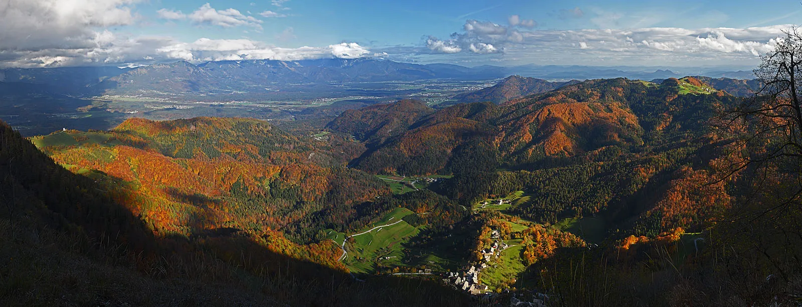 Photo showing: This is the view from Bela skala, the edge of Pokljuka plateau, over Gorenjska plane. Below is the village of Podblica, far on the left is the famous church of St. Primus, left in the distance are Kamnik and Savinja Alps (in clouds).