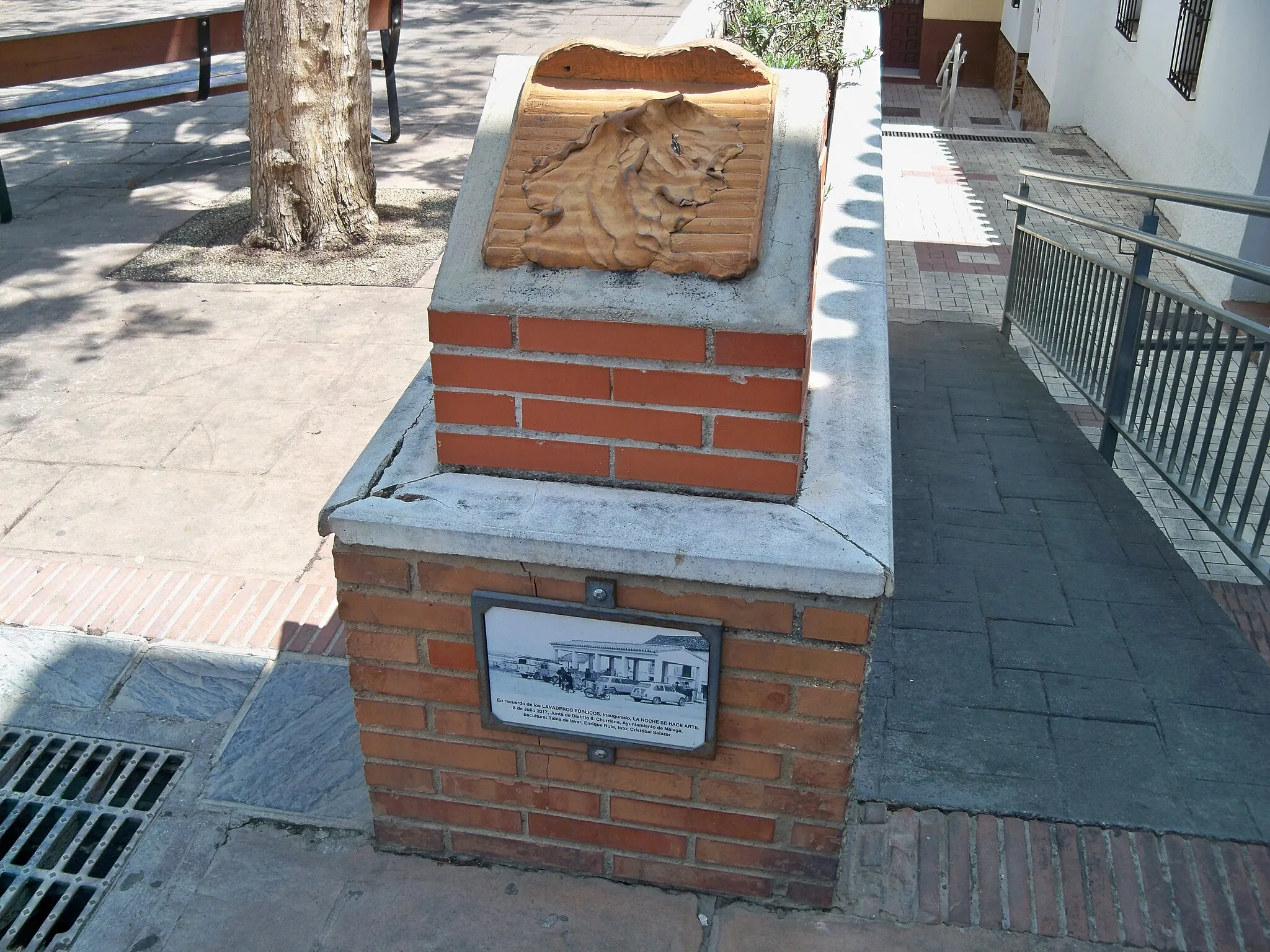 Photo showing: Monumento a los lavaderos públicos, en el distrito de Churriana, Málaga, España. En la base del monumento se sitúa una placa donde, junto a una fotografía de un lavadero público, dice: «En recuerdo de los lavaderos públicos. Inaugurado, LA NOCHE SE HACE ARTE. / 8 de julio de 2017, Junta de Distrito 8. Churriana. Ayuntamiento de Málaga. / Escultura: Tabla de lavar, Enrique Rute, foto: Cristóbal Salazar». La propia escultura luce una inscripción donde se lee: «A ti mujer / que / mueves / el / mundo».