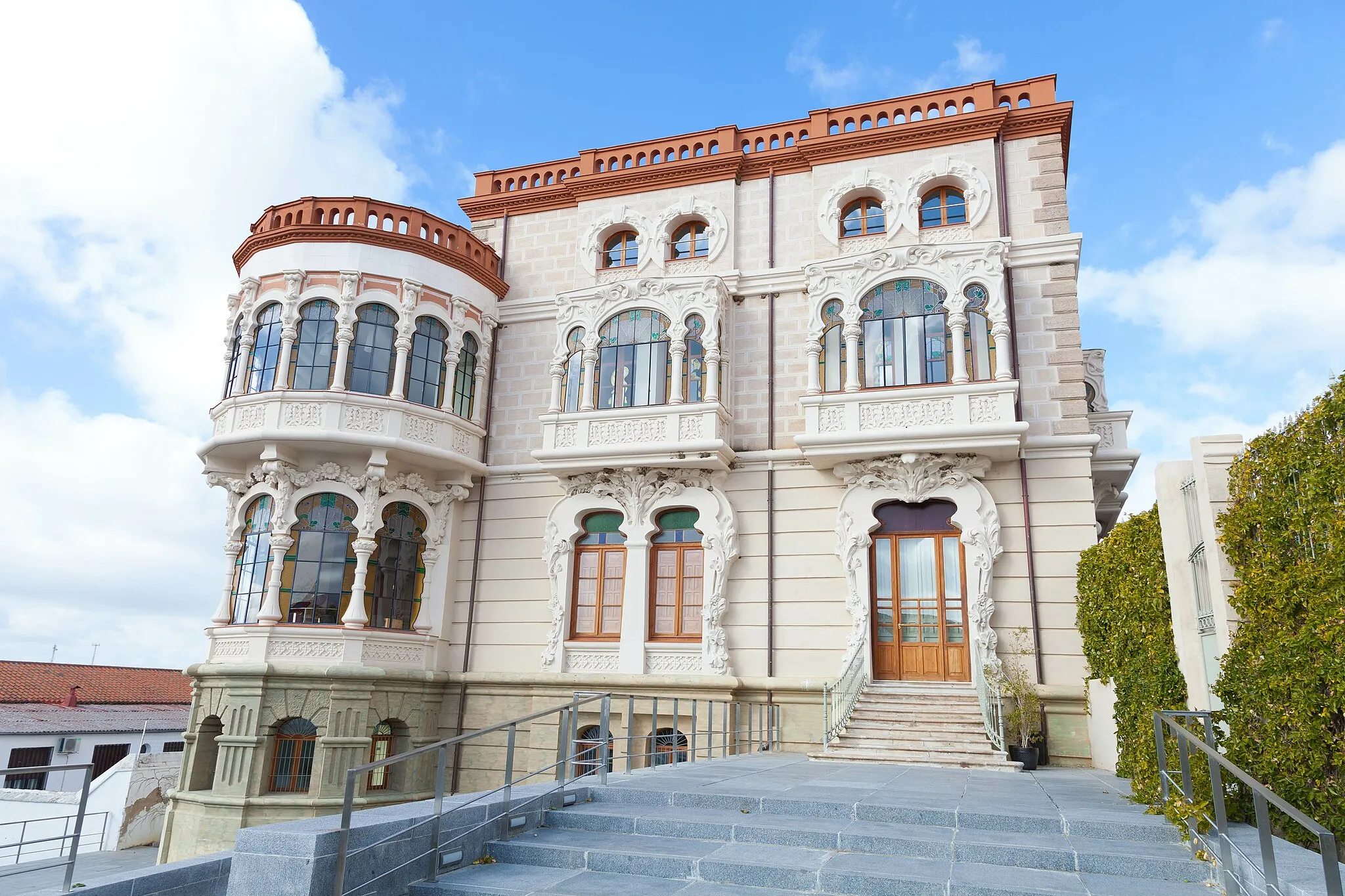 Photo showing: Palacete Modernista:
Fuente Obejuna cuenta entre su singular patrimonio arquitectónico con un ejemplar magnífico de la arquitectura modernista, desarrollado en España a finales del siglo XiX y principios del XX.
Este singular Palacete Modernista, también conocido como "Casa Cardona", fue mandado a hacer por D.Pedro Celestino Romero de Santos.
En altura, el edificio consta de una planta baja, piso principal y un segundo piso, además de sótano y azotea superior.
Las fachadas concentran su decoración en puertas, ventanas y balcones; quedando limitado el resto a franjas horizontales destacadas por hendiduras de fondo plano en la planta baja, principal y alta, simulando sillares dispuestos a soga. El edificio es cornado por el barandal de la terraza, evocando una crestería calada de huecos verticales con extremos semicirculares.
La portada está organizada perfectamente según un eje de simetría desarrollando lineas curvas, circulares y parabólicas.
no debemos olvidar, que su cubierta (central) está compuesta de cristales, que permiten la iluminación principal en su interior y mediante un sistema de aberturas la ventilación de la casa.
En sus dependencias se encuentran ubicadas la Oficina de turismo y el Museo Histórico Municipal.

Edificio visitable donde se encuentra la Oficina de Turismo de Fuente Obejuna tel: 699 651 210