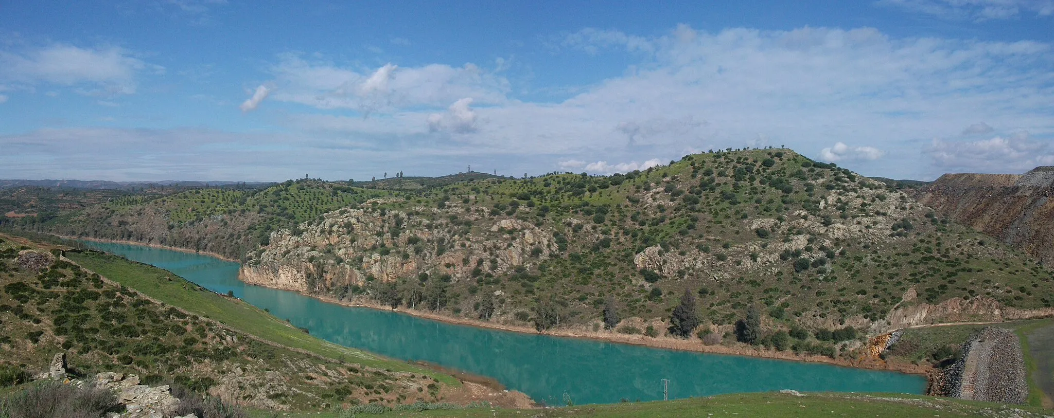 Photo showing: Rio Agrio a la altura del casco municipal de Aznalcóllar que queda a la izquierda de la imagen y fuera de ella. A la derecha están las escombreras de las antiguas minas de pirita. El color turquesa es debido a la contaminación residual que proviene de las escorrentias de las escombreras.