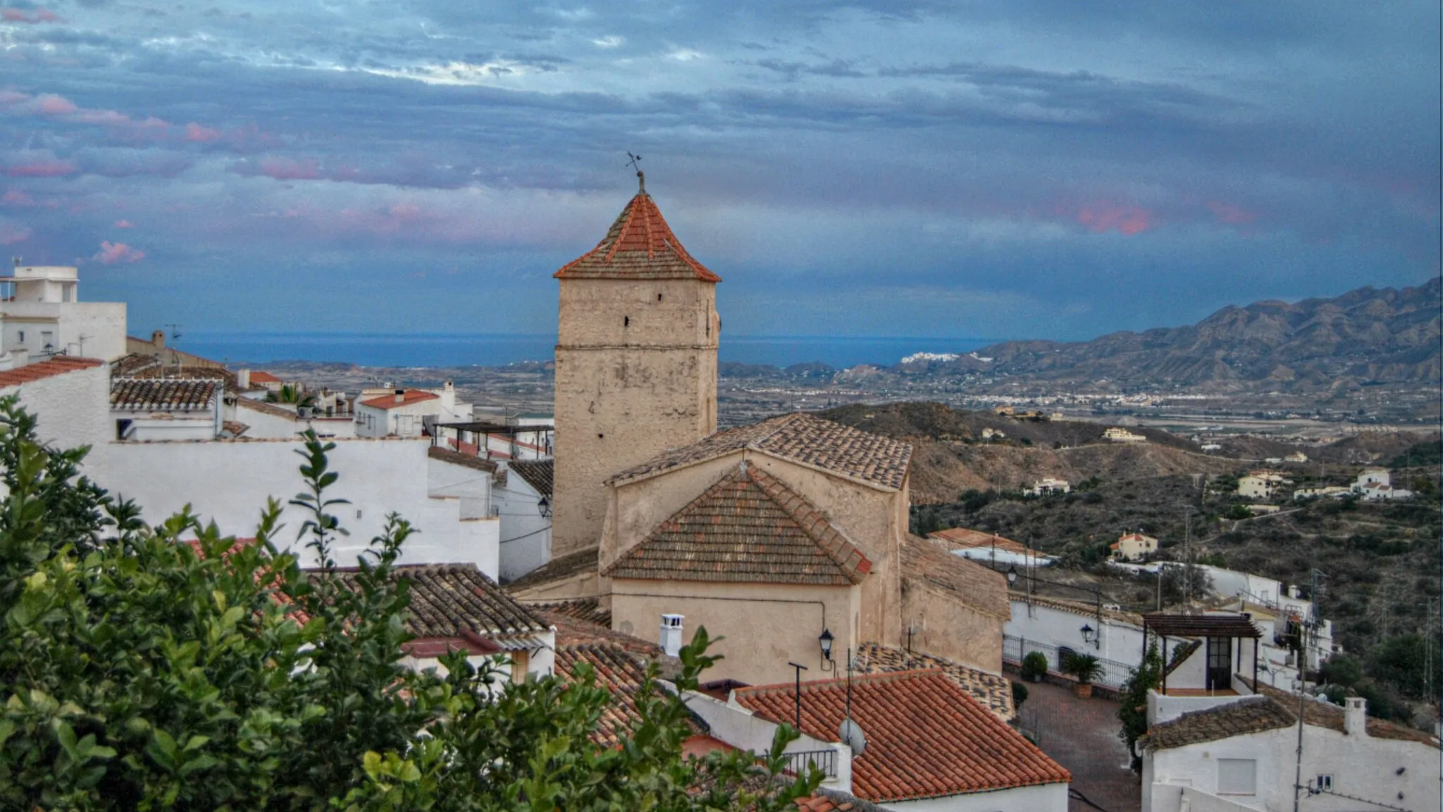 Photo showing: The parish church Iglesia Santa Maria de la Cabeza can be spotted above the village house rooftops, it is located in the Plaza Santa Maria, inside the church there are two oil paintings, one of San Gregorio and the other of the Virgen de la Cabeza, both being the patron saints of the pueblo. Just to the right of the church can be seen the town of Mojacar nestled in the mountains.