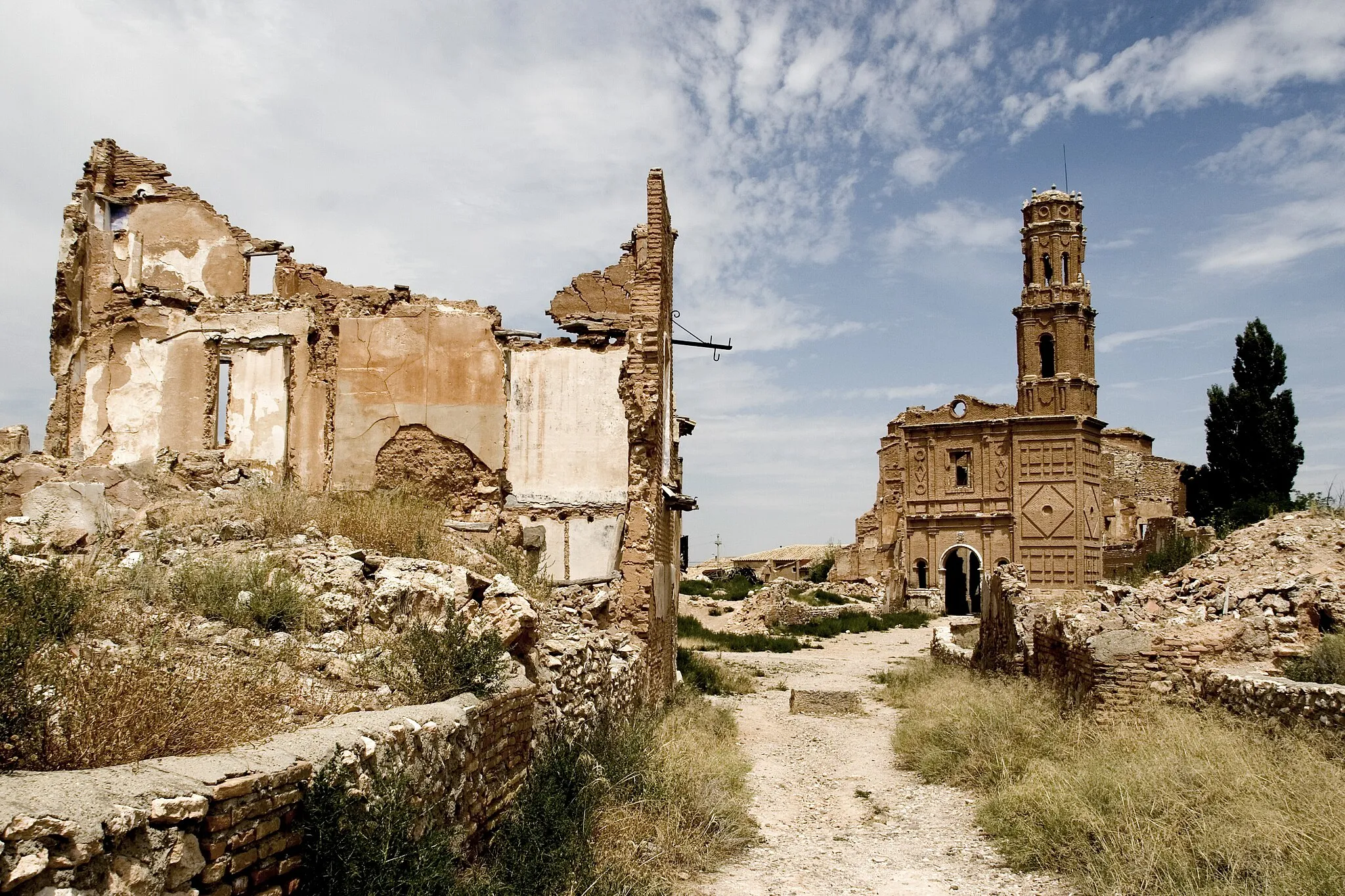 Photo showing: En plena Guerra Civil, Belchite fue el escenario de una de las batallas más crueles de toda la contienda, pues por su importancia y localización era una pieza vital en la estrategia de avance de los ejércitos de ambos bandos.
En agosto de 1937, el ejército republicano lanzó una gran ofensiva en la zona. Su principal objetivo, la toma de Zaragoza. Pero Belchite, que se había sublevado contra la República y situado a favor del bando nacional, se interponía en el camino, y no era una población precisamente desdeñable.
El ejército republicano se abalanzó sobre el pueblo con más de 8.000 hombres, carros de combate y bombarderos. Belchite se disponía a pasar los días más dramáticos de su larga historia.
Gracias a la elevada moral de sus habitantes y a que disponía de abundantes fortificaciones defensivas de la época de los árabes, Belchite planteó una resistencia que jamás imaginaron los atacantes.
Trece días de asedio, trece días de lucha cuerpo a cuerpo, casa por casa, trece días de bombardeo incesante de aviones y artillería bastaron para convertir Belchite, la hermosa villa de más de 2000 años, en un amasijo de escombros, muerte y espanto.
Y tras esos trece días, el 6 de septiembre de 1937 fue tomada por los republicanos. Seis meses más tarde, las tropas de Franco volvieron a conquistar definitivamente el pueblo; después sólo quedaría el desastre y la destrucción, el estéril sacrificio de tantas vidas y el dolor lacerante para los supervivientes de ambos bandos.
Franco mandó construir un pueblo nuevo en la ladera opuesta de la colina que ocupaba el pueblo viejo, y ordenó que no se tocara ni una piedra del viejo Belchite como símbolo de su victoria y para que nadie olvidara la gesta de sus habitantes.
En las proximidades se construyeron las naves que serían el campo de concentración hacia donde fueron trasladados los presos del bando republicano. Allí, en condiciones infrahumanas y sometidos a trabajos forzados, fueron utilizados como mano de obra gratuita para levantar el pueblo nuevo.
Hoy en día, el pueblo viejo de Belchite es una silueta fantasmal. Sólo algunos pastores lo atraviesan con sus rebaños, buscando algo de alimento en este sediento secano hacia las cañadas que durante siglos atravesó la trashumancia.

Fuente: www.quesabesde.com/noticias/fuendetodos-goya-belchite-gue...