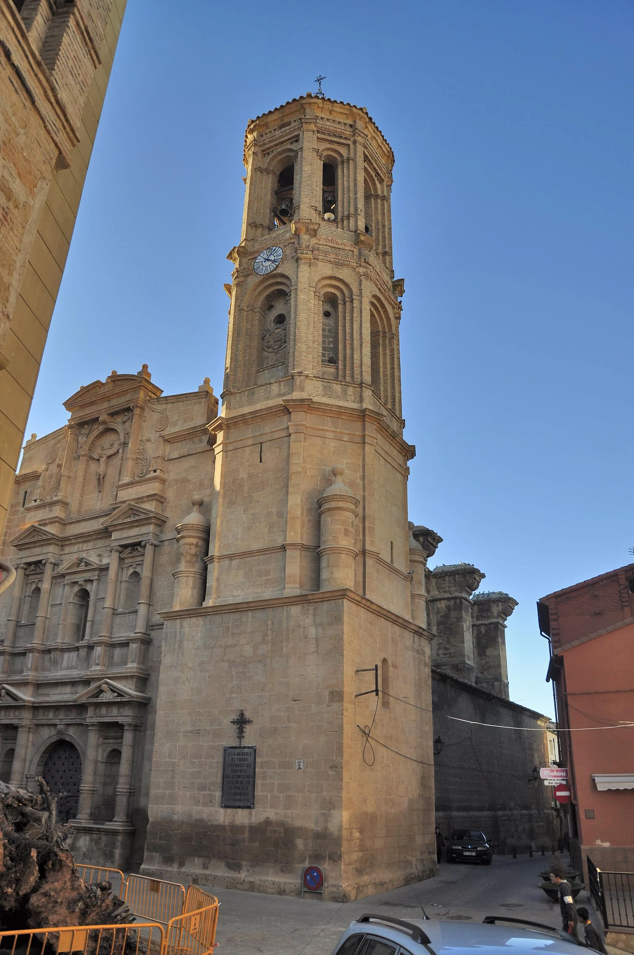 Photo showing: Se trata de un edificio de notables dimensiones, de nave única
con capillas entre los potentes contrafuertes y cabecera recta
al exterior y poligonal al interior. Fue construida entre finales
del s.XVI y principios del s.XVII siguiendo un proyecto unitario.
La fábrica está realizada en sillar de piedra arenisca, a excepción
de la torre situada en el ángulo suroriental, que combina
el sillar en sus dos cuerpos inferiores con el ladrillo en los dos
superiores, fruto de una ampliación de mediados del s.XVII.
En esta torre se combinan la planta cuadrada del primer cuerpo
con la octogonal de los restantes, haciéndose la transición
por medio de torreoncillos de ángulo. Asimismo se combinan
elementos de un incipiente barroco con otros de tradición mudéjar.
Al exterior destaca la fachada monumental realizada en clave
manierista. Se trata de una portada-retablo articulada en dos
pisos separados por un entablamento y coronados por un ático
cerrado por un frontón mixtilíneo que cobija la imagen de

un crucificado.