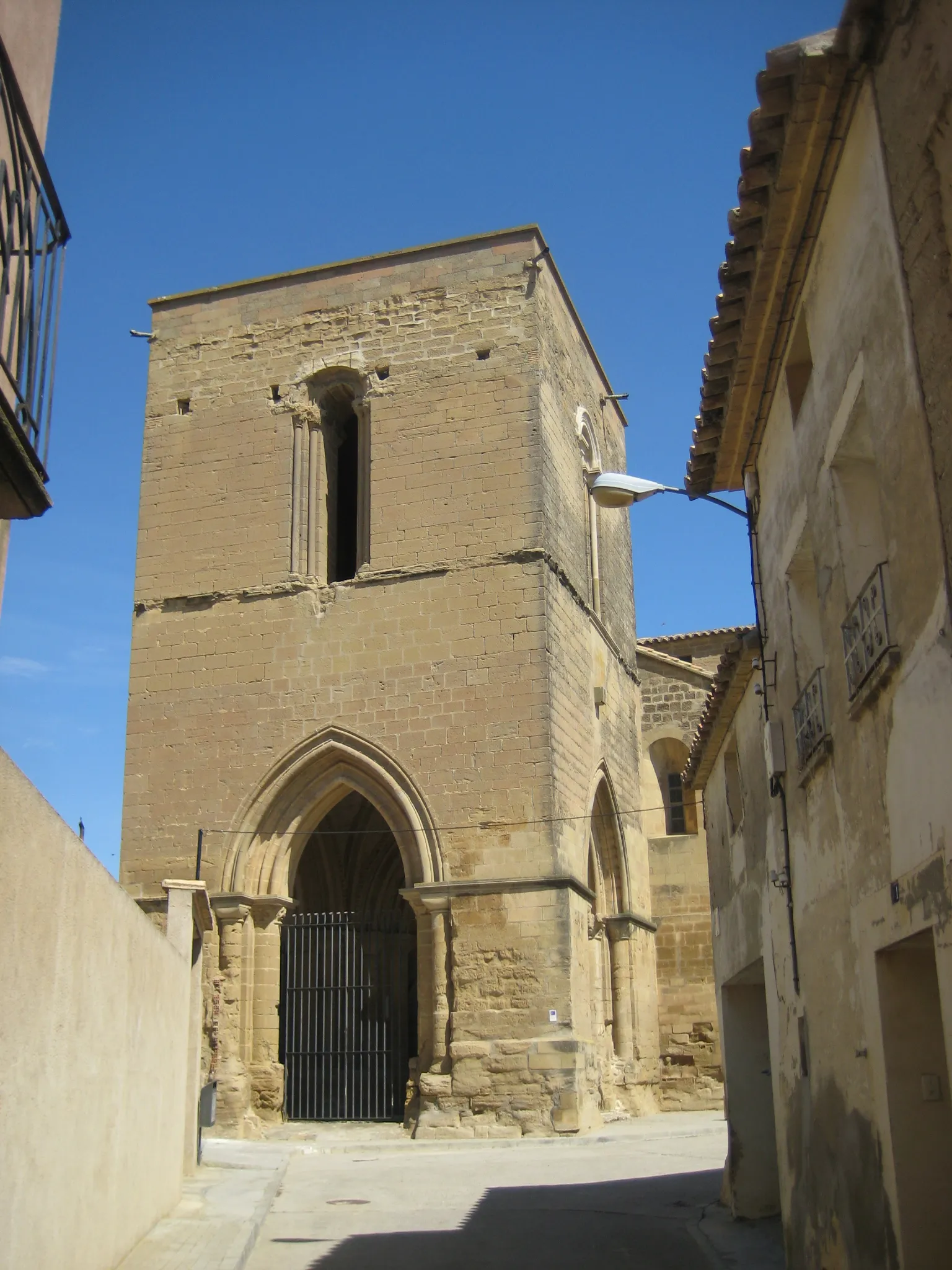 Photo showing: Se trata de una iglesia construida en el s.XII en estilo románico
tardío, que debido a su importancia llegó a ostentar el rango
de colegiata. Su fábrica es de sillar y actualmente se encuentra
exenta.
Consta de tres naves y cabecera triple con ábsides semicirculares
cubiertos por bóveda de horno. Las naves se cubren con
bóvedas de cañón y el crucero, no marcado en planta, con
bóveda de crucería estrellada del s.XVI.
También de época renacentista data la construcción del coro
alto situado a los pies de la nave central y de la capilla de San
Pedro Arbués, situada junto al coro.
Su portada principal se abre en el muro septentrional y junto a
ella existe una ventana sobre la que hay embutido un tímpano
tallado con un Pantocrátor rodeado por el Tetramorfos y un
crismón trinitario.
En el muro meridional se encuentra adosado un gran atrio
abierto por medio de tres arcos apuntados y cubierto por una
bóveda de crucería sencilla. Las columnas situadas en los ángulos
del atrio presentan bellos capiteles historiados.
Sobre este atrio se alza una magnífica torre del s.XIII, de planta
cuadrada y dos cuerpos en altura rematados por una terraza
plana.

Entorno