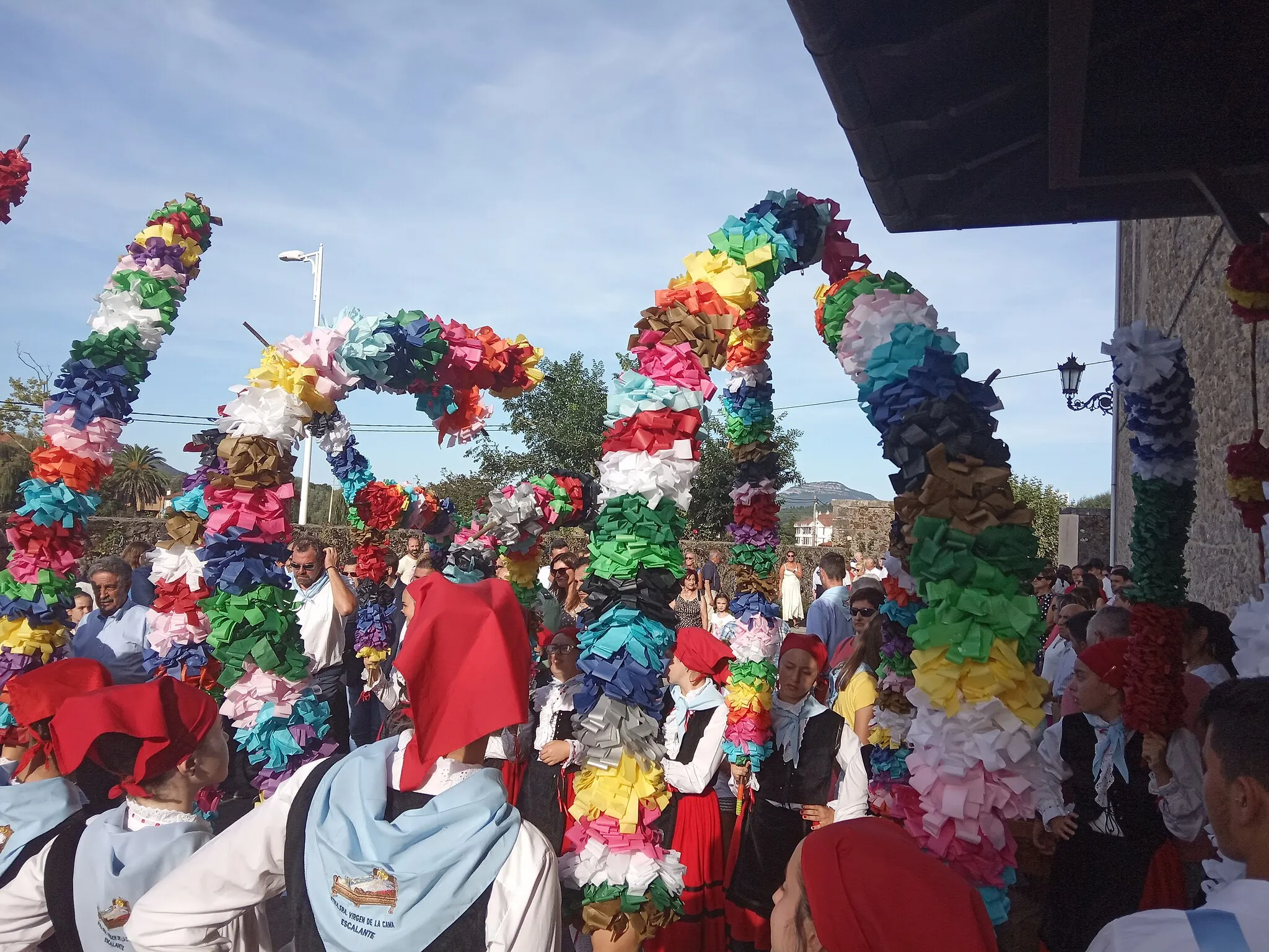 Photo showing: Danzantes vestidos con los trajes tradicionales del pueblo de Escalante y el pañuelo de la festividad de la Virgen de la Cama que sujetan arcos de flores de distintos colores y están a la espera de la salida de la virgen para comenzar la procesión en su honor.