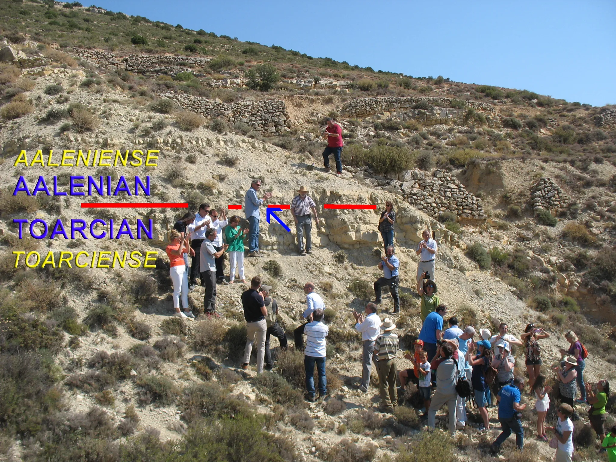 Photo showing: Aalenian GSSP (Lower-Middle Jurassic boundary). Golden spike ceremony: July, 28th 2016. Fuentelsaz, Guadalajara, Spain. Toarcian-Aalenian boundary overprint. The blue arrow points to the golden spike. Beside the golden spike are, at the left, Dr. Stanley Finney (President of the International Stratigraphic Commission) and, at the right, Dr. Antonio Goy Goy (Professor Emeritus of the Faculty of Geological Sciences at the Complutense University of Madrid).