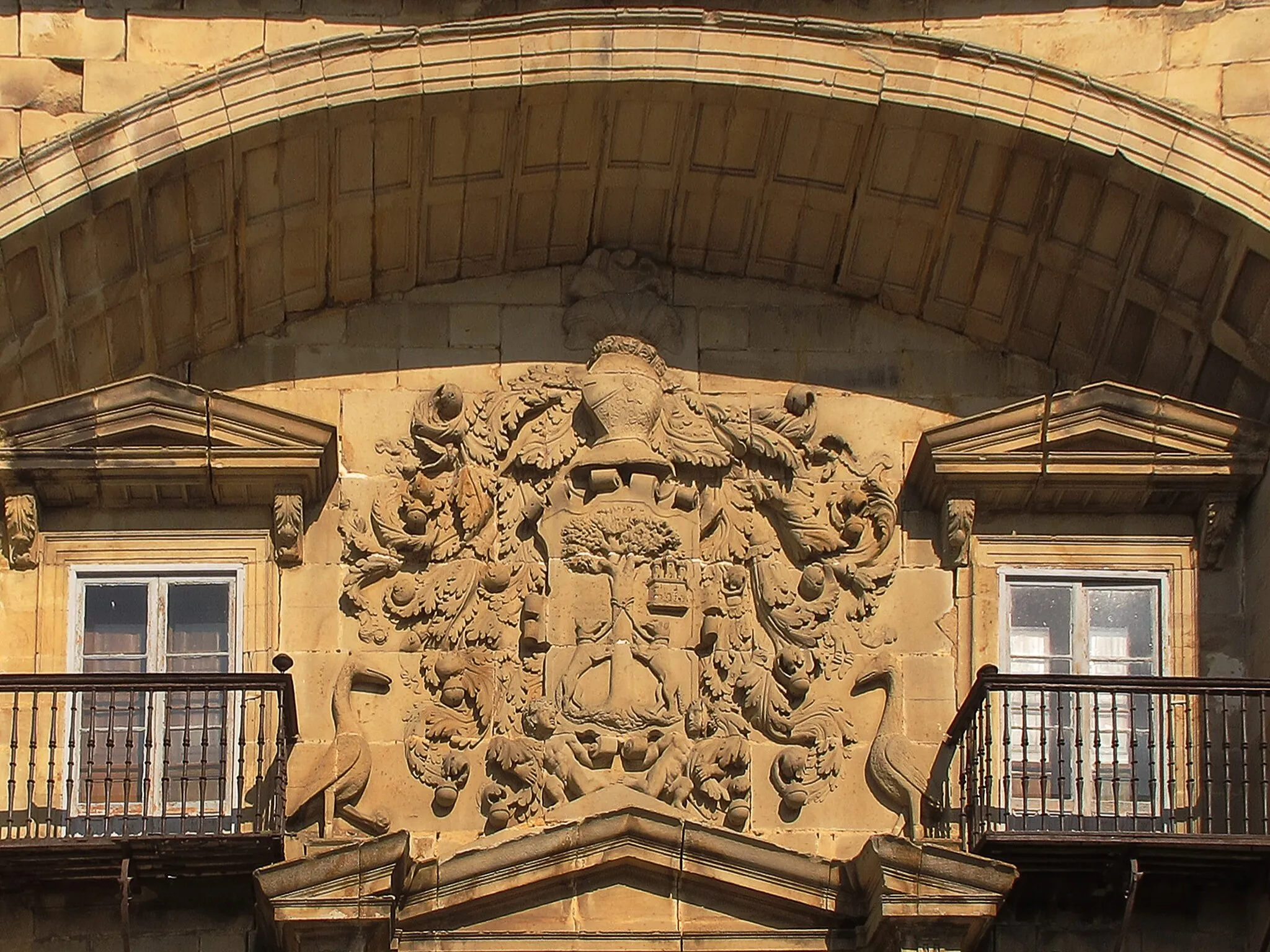 Photo showing: Palacio de Chiloeches (Espinosa de los Monteros)
Las Merindades de Burgos
Está situado en mitad de la Plaza de Sancho García en Espinosa de los Monteros, y aunque todos lo conozcamos con el nombre de los Marqueses de Chiloeches, eso no fue siempre así. El palacio se construyo a finales del S. XVI y 
principios del XVII, sobre una edificación anterior.
La parte del palacio entre las dos grandes torres cuadradas, sirven de marco y punto de máxima atención del cuerpo central, y se remata en un arco escarzano que cobija el monumental escudo y la cuidada portada.
La piedra no expresa los colores que son estos: campo de oro para una encina verde y dos zorros negros, y un campo azur para una torre plata.
El escudo es impresionante, no es que destaque en la fachada, lo hace, sino que destaca en toda la plaza de Sancho García. Sobre una cama de Lambrequines (adornos como hojas o jirones de tela) con cascabeles aparecen las armas de los Zorrilla enmarcadas con burletes (cintas trenzadas o especie de rodillos). El escudo está sujeto por dos tenantes (figuras humanas que lo aguantan), rematado por un yelmo florido con la celada bajada, rodete (cinta de tela de colores) y penacho. 
Finalmente, el conjunto recibe la ayuda de dos garzas que actúan como soportes.
En los escudos de esta familia en Espinosa se pueden ver dos zorras afrontadas al tronco de un árbol y atadas con una cuerda por el cuello, y en la parte superior derecha aparece 
un castillo.
El escudo pertenece a la familia Zorrilla de San Martín proveniente de San Martín en Soba, lugar donde habían fundado mayorazgo en 1535. Y encuentra entre los escudos más grandes de Burgos y de Castilla y León. 
Existe en torno a 1588 una Ejecutoria del pleito, litigado por Juan Zorrilla de San Martín y Francisco Zorrilla de San Martín con Juan de Bueras y Juan de Bueras de la Torre, escultores, vecinos de Bueras (Cantabria), sobre el pago del escudo de armas que habían esculpido para la casa de los Zorrilla. (Archivo de la Real Chancillería de Valladolid ,REGISTRO DE EJECUTORIAS,CAJA 1623,42)

Como suele ser habitual los mayorazgos cambian de familia por casamientos herencias, etc. y en este caso con el tiempo el palacio recayó en una mujer casada con un Porres, por eso los actuales dueños llevan ese apellido. En el S. XIX adquirieron el titulo de Marqueses de Chiloeches que es como actualmente se conoce el edificio. A finales del S. XIX D. Luis de Porras restauro el edificio
El palacio también es conocido como “El Fuerte”, ya que durante la Guerra de la Independencia y las Guerras carlistas fue utilizado como acuartelamiento de mandos o de tropa.
Bienes de interés cultural de la provincia de Burgos
En 1921 en el "Escudo de la Familia Zorrilla." " se añadio un lema por el hijo del poeta Juan Zorrilla de San Martin descendiente de Juan Zorrila San Martin "el viejo" (1488)
"Velar se debe la vida, de tal suerte... que viva quede en la muerte"...
Es un soberbio ejemplar heráldico, muy vistoso desde un punto de vista artístico, pero no del todo ortodoxo en el aspecto heráldico, pues las armas genuinas de los Zorrilla de San Martín consisten en un escudo partido, en cuya primera partición aparece una encina verde en campo de oro con dos zorras negras empinadas y atadas al tronco; mientras que la segunda partición trae un castillo de su color en campo azul. Añade una orla de oro con la siguiente leyenda en letras de sable «velar se debe la vida de tal suerte, que viva quede en la muerte».
Por último, el escudo ha de aparecer soportado, como ocurre aquí, por dos grullas de su color, cada una de ella con un pie en alto que sostiene una piedra (símbolo de vigilancia).
En este ejemplar, el artista ha suprimido la segunda partición, si bien ha incluido el castillo, reducido en tamaño, en el cantón siniestro, y ha suprimido también la bordura con la leyenda.
Ello no obstante, las armas resultan plenamente reconocibles..... Faraute1
Una leyenda en el primer comentario

Se trata de adivinar el lugar de la fotografia.......