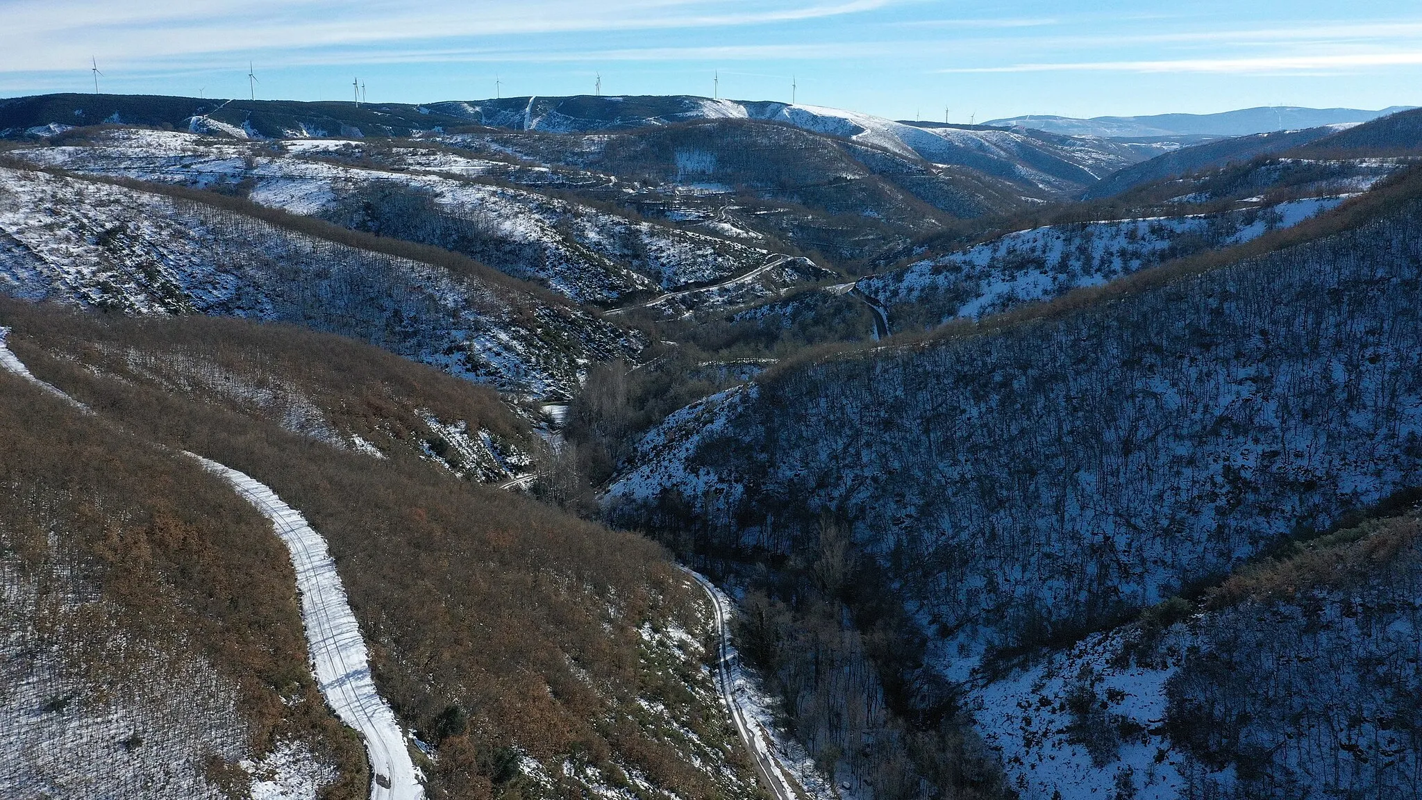 Photo showing: Paisaje nevado en Rodrigatos de las Regueras, Igüeña (León, España). Vista aérea del valle del río Rodrigatos, hacia el Sur. Se observa la carretera LE-4311, la población de Rodrigatos de las Regueras y aerogeneradores en el camino de Villagatón.