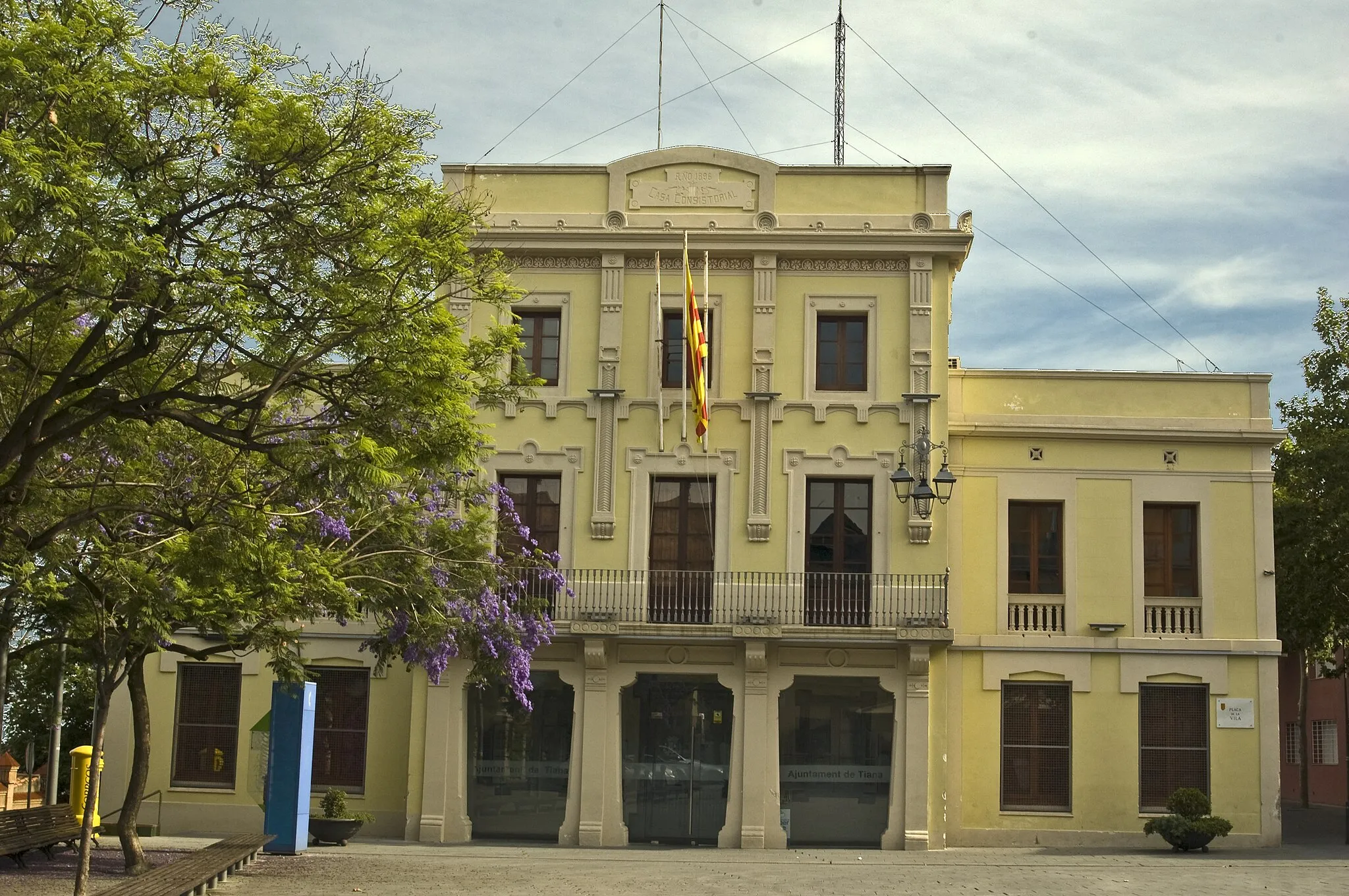 Photo showing: Ajuntament (Tiana). Edifici eclèctic de finals del S.XIX, es va començar a construir el 1890 quan era alcalde en Pere Cruspinera Barnadàs. El mestre d'obres va ser n'Isidre Reventós i Amiguet (Barcelona 1849-Juliol 1911). En un principi va ser seu consistorial i escola de nens i nenes. Té dos cossos laterals de planta baixa i pis i un cos central més alt, més ornamentat que els altres dos.