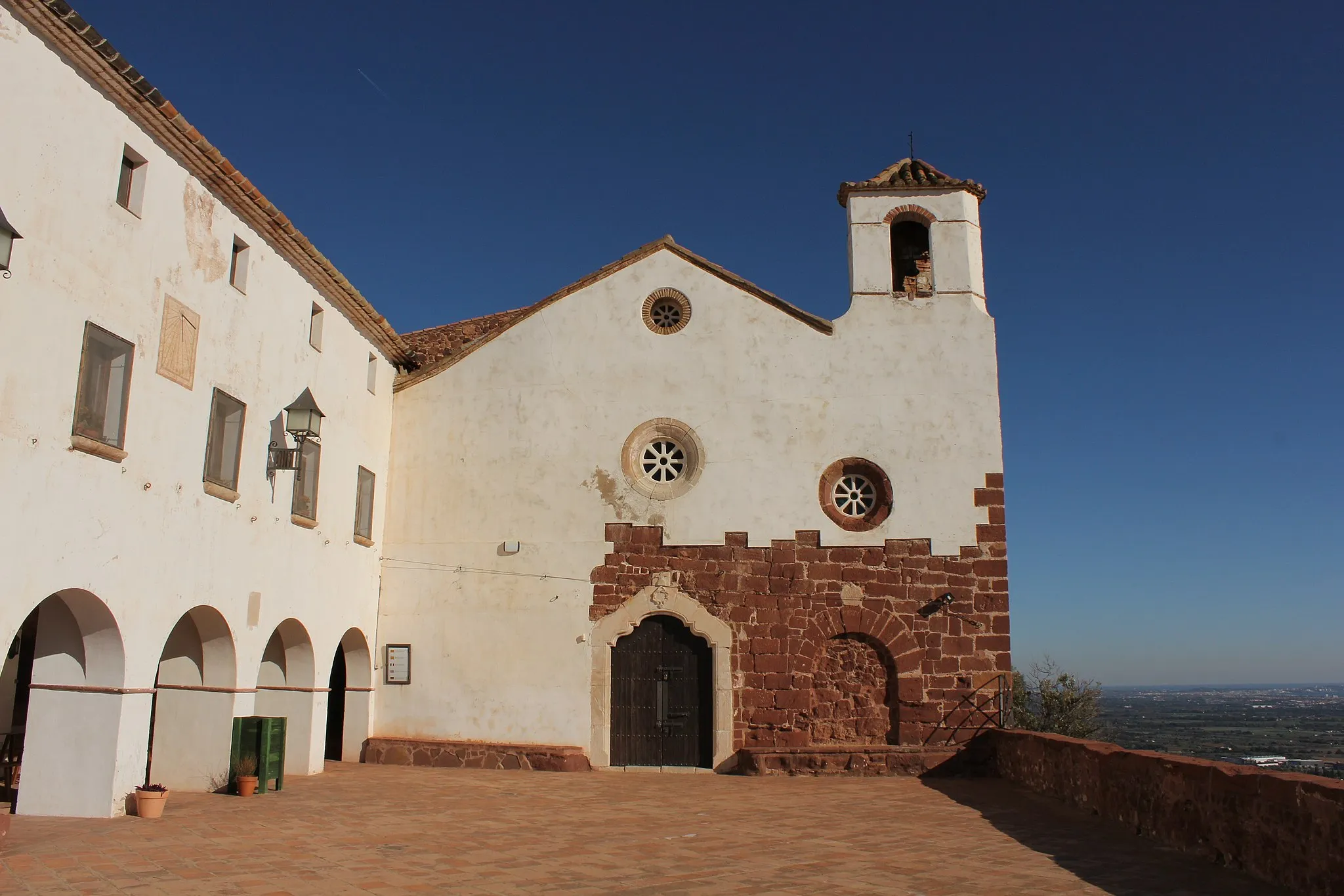 Photo showing: L'Ermita de la Mare de Déu de la Roca és una ermita situada a Mont-roig del Camp (Baix Camp). Es troba a 294 msnm damunt una roca molt erosionada.
El santuari marià està situat al cim d'una roca que s'alça a l'oest de la vila, que l'erosió ha configurat d'una manera característica. Està orientada a ponent, amb unes mides de 20x7 metres, sense comptar les capelles laterals, i té la façana arrebossada. Al davant hi ha una petita plaça porticada.
És una petita capella d'una sola nau quadrangular, feta amb carreus, en part excavada a la roca de pedra sorrenca vermella. Té un petit campanar cec als peus. La capella té un cor alt als peus i un cambril a la capçalera amb la imatge de la Verge.
En una restauració recent, s'ha posat al descobert una part de la façana, amb una porta cegada, amb arc rodó adovellat, de l'any 1655, al costat esquerra de la porta d'entrada a la capella (centrada respecte a la façana), que porta la data de 1785.
Seguint un passadís que passa pel "Fossar de les Monges" (on no s'han trobat restes humanes), es puja per uns graons tallats a la mateixa roca, a una petita capella rectangular, sense decoració, dedicada a Sant Ramon, situada al cim d'una roca molt erosionada en la base.
S'han trobat restes de ceràmica ibèrica al fer-se una placeta i una font sota l'ermita.
L'existència de l'ermita està documentada en un testament atorgat el 12 de maig de 1299. Hi ha una llosa al pòrtic de la placeta amb l' inscripció "B(eata). M(aria). Giberga. Me. Fecit. Ann(orum) 1591".
Als peus de l'església, hi ha una llosa funerària amb la data de 1737. Després de la guerra del francès, l'any 1814, es va reconstruir. La imatge de la Verge amb el nen, de fusta ennegrida, sembla del segle XVIII.
Sembla que del 1439 al 1835 en tingueren cura els frares d'Escornalbou i una tradició no provada hi esmenta un convent de benedictines. Segons la tradició la imatge original, destruïda el 1936, havia estat trobada per un pastor sota una palmera.
Damunt l'ermita de la Roca hi ha la capella de Sant Ramon, emblanquinada per servir de guiatge als mariners; la imatge del sant havia estat trobada a la mar i la primera capella fou construïda vers el 1826. Fou restaurada el 1902 per un grup de dones de Mont-roig i els reusencs Miquel Herrero i Prudenci Anguera. Des de la capella es domina una extensa i bella panoràmica.

ca.wikipedia.org/wiki/Ermita_de_la_Mare_de_Déu_de_la_Roca