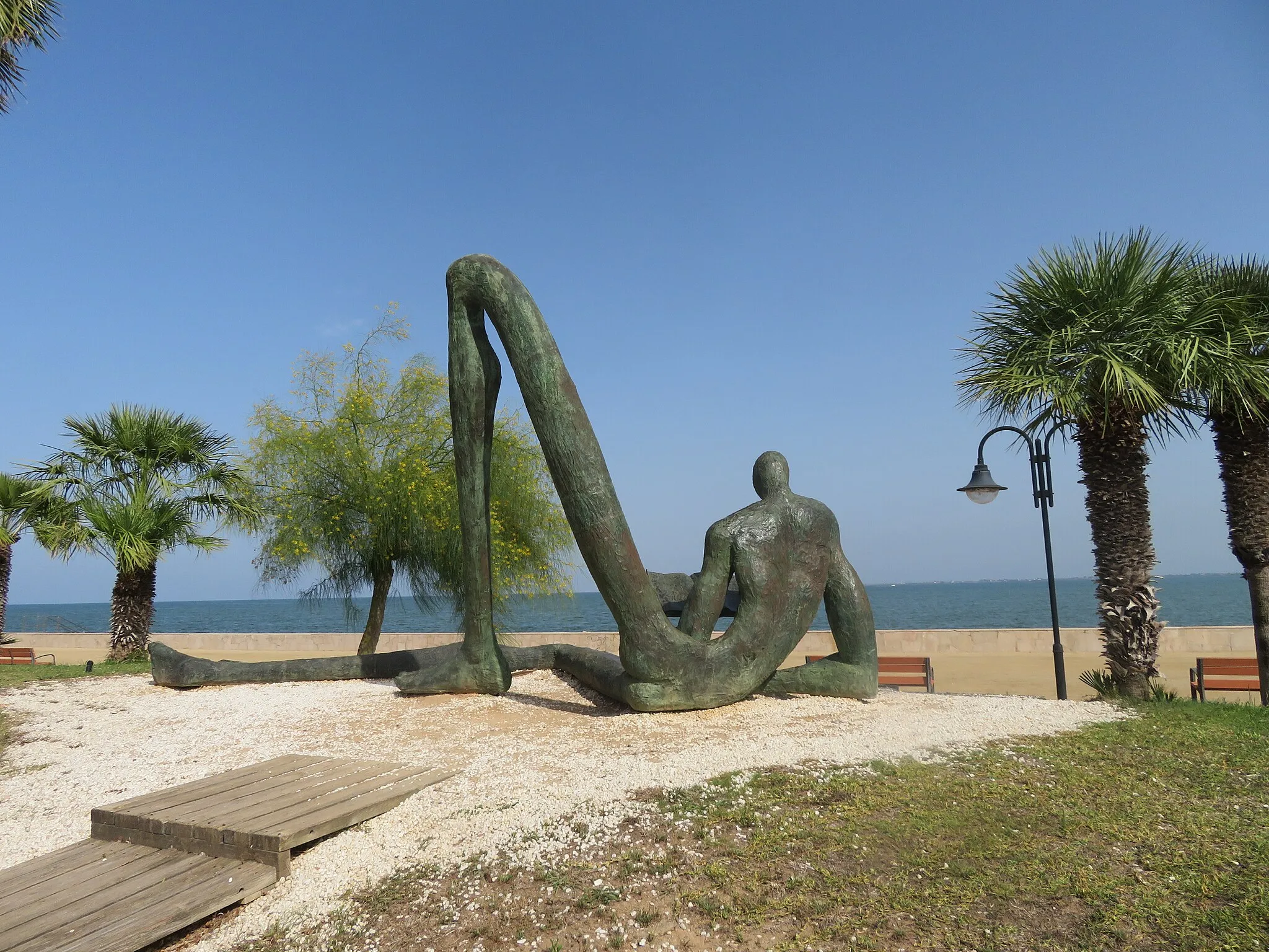 Photo showing: Arte urbano. Escultura de bronce titulada “El lector de l’Odissea” se localiza en el Paseo del Arenal (Passeig de l’Arenal de l’Ampolla) y fue realizada por el escultor Paco Morales en el año 2000. Este enorme bronce representa a un hombre esquematizado leyendo simbólicamente el libro de l’Odissea de Homero sentado tranquilo junto al mar.