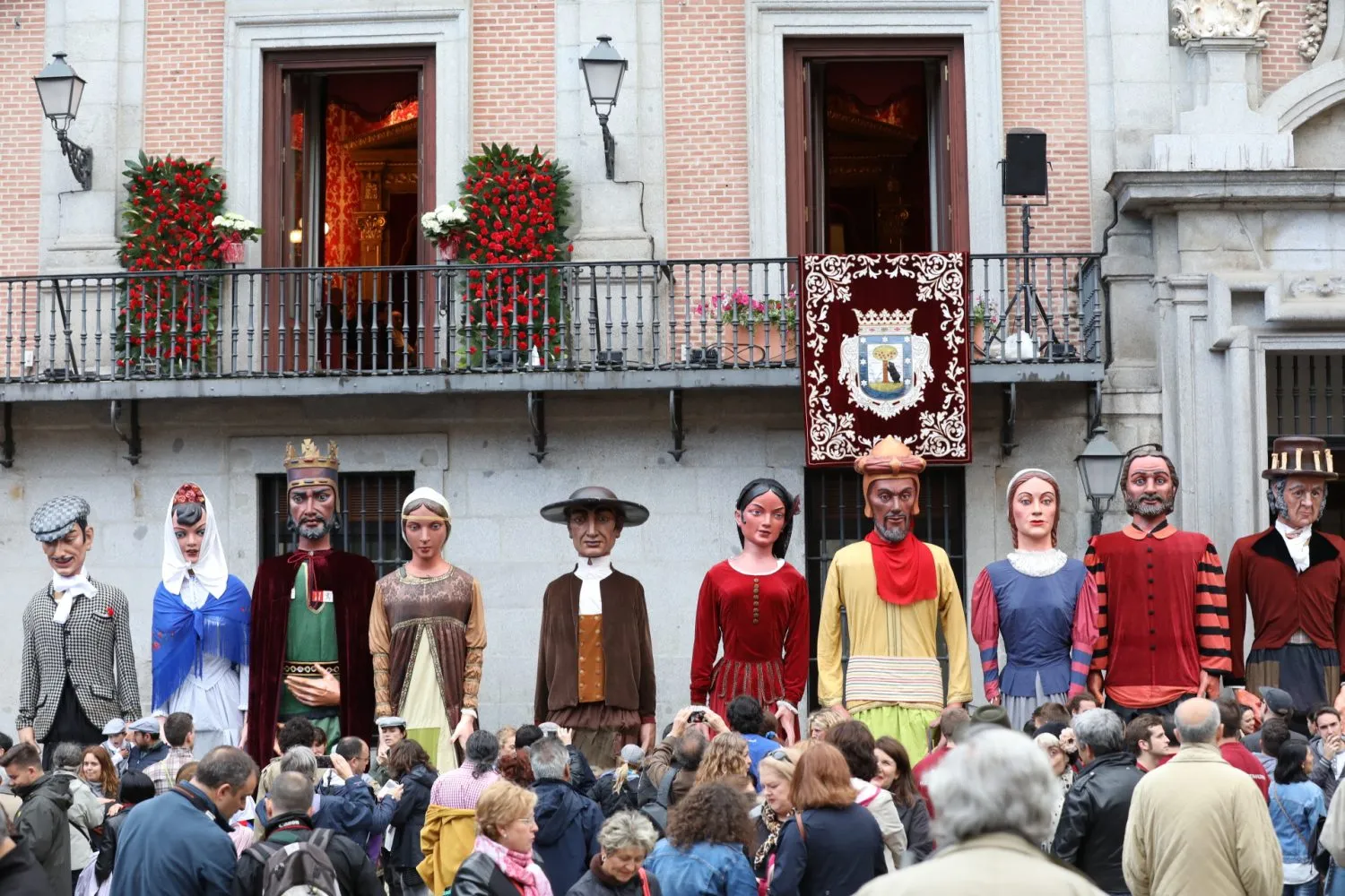 Photo showing: Desde el balcón del número 5 de la Plaza de la Villa, la alcaldesa de Madrid, Manuela Carmena, y el pregonero de San Isidro 2017, el periodista, escritor y humorista Juan Luis Cano, han inaugurado esta festividad. La alcaldesa no dejó pasar la ocasión para destacar el perfil de persona sencilla del patrón de Madrid: “San Isidro no fue obispo, ni mártir, ni virgen. Fue un señor corriente como el que ahora podríamos encontrarnos en un bar o quizás en la cola del paro”. También recordó su profesión de campesino y su vinculación con lo ecológico y el medio ambiente, para invitar a la ciudadanía a comprometerse con “un Madrid sin contaminación y más natural”.
Antes de la cita con el pregonero Juan Luis Cano, la Comparsa de Gigantes y Cabezudos de la Ciudad de Madrid ha desfilado por céntricas calles de la ciudad. Este festivo pasacalle partió a las 18 horas desde la plaza de Santo Domingo. En su recorrido por la plaza de Callao, la calle Preciados, la Puerta del Sol y la calle Mayor hasta llegar a la plaza de la Villa, han estado animados por las chulapas y chulapos que se sumaron al desfile festivo. La Comparsa de Gigantes y cabezudos celebra su 50 aniversario este año. Por este motivo, la alcaldesa Manuela Carmena ha felicitado a la tradicional comparsa en sus 50 años de vida, efeméride que celebrarán mañana sábado a las 11 del mediodía con una foto de familia en la plaza Mayor.

Por su parte, Juan Luis Cano ha dado arranque a las fiestas con un pregón en verso en el que ha felicitado y animado a todos los distritos a disfrutar de las fiestas patronales de Madrid. Con el humor que le caracteriza, y reconociendo en los primeros versos la emoción y los nervios por convertirse en el pregonero de San Isidro, se ha felicitado por la diversidad de la programación y ha invitado a disfrutarla pidiendo que seamos capaces de mantener la ciudad limpia durante estos días. También ha hecho guiños a la actualidad de la ciudad y a los iconos clásicos madrileños para cerrar con una llamada a disfrutar de Madrid en fiestas.